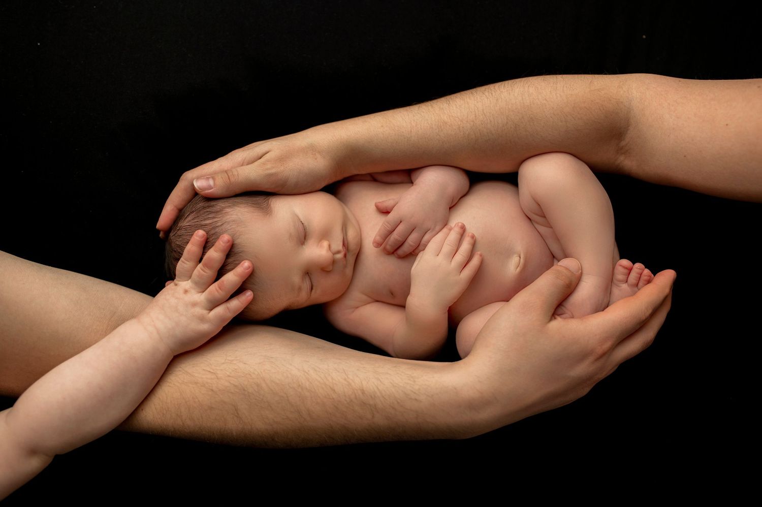 Newborn baby resting in protective hands against dark background in tender portrait.