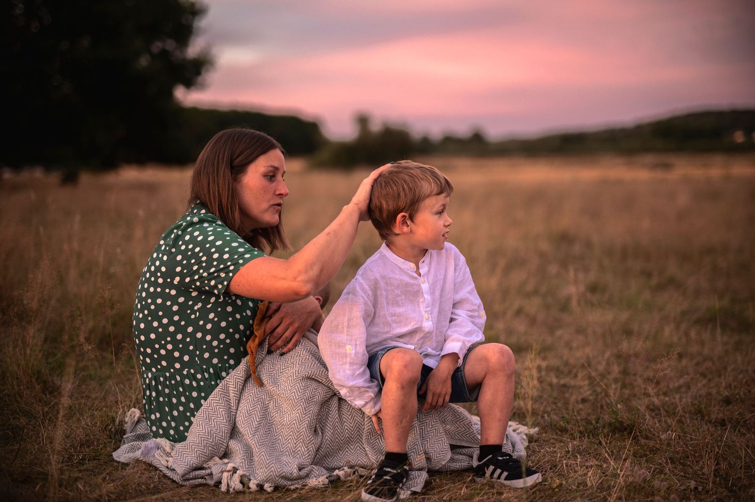 Person in polka dot dress sitting with companion on grassy hill at dusk.