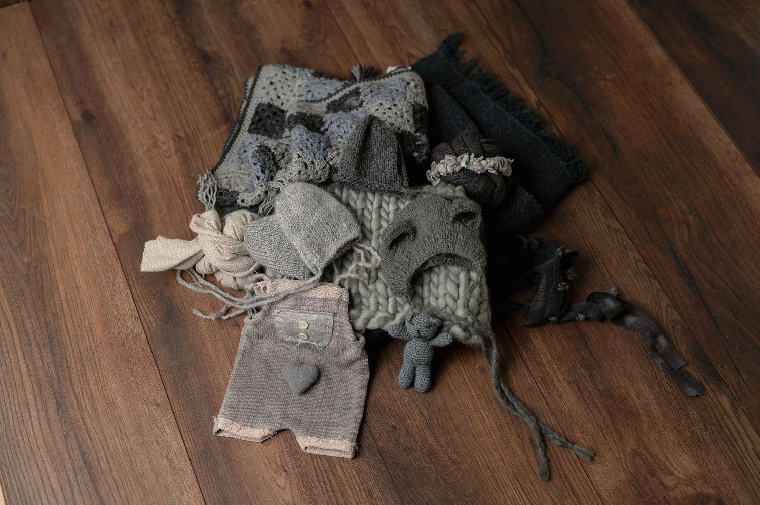 Assorted gray and neutral colored baby clothes and accessories arranged on wooden flooring.