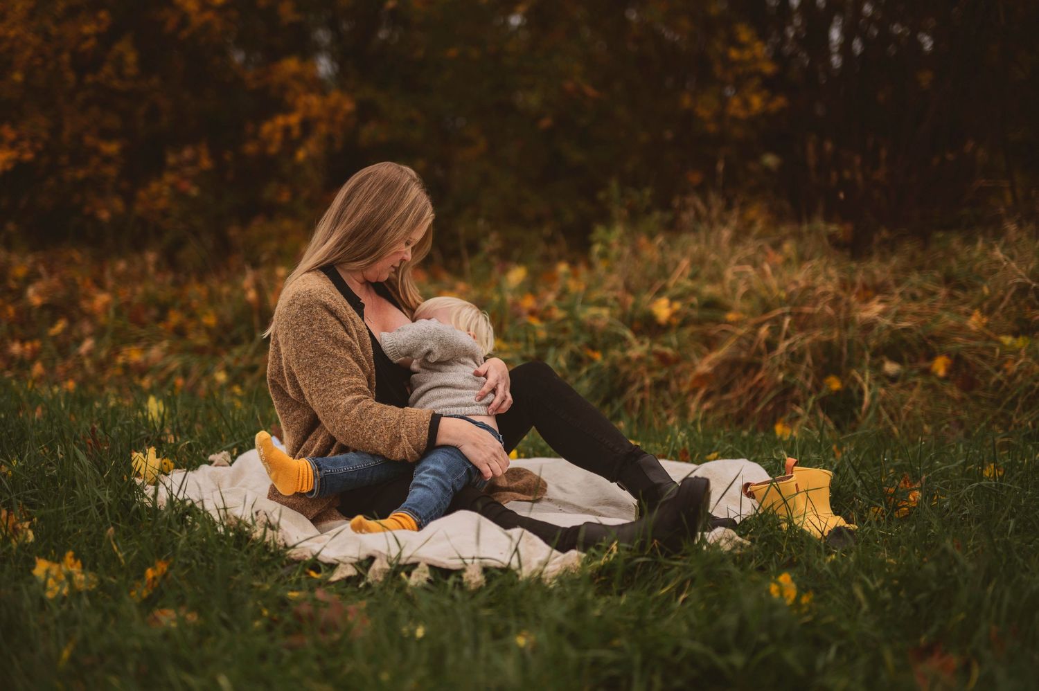 Cozy autumn picnic scene on a blanket with yellow boots in a field of fall leaves.