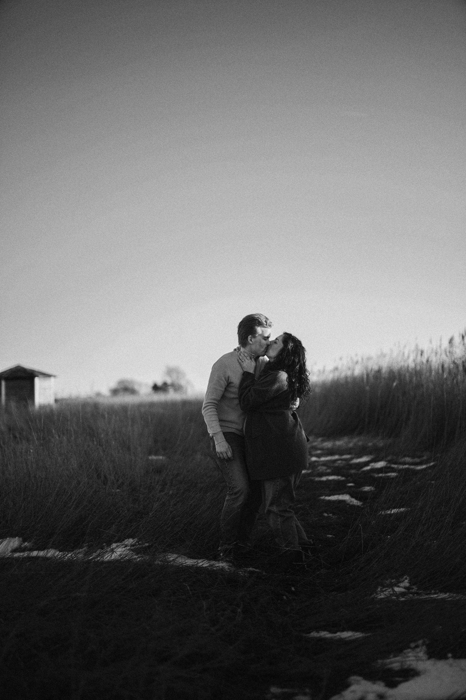 Black and white silhouette of a couple embracing on a path surrounded by tall grass.