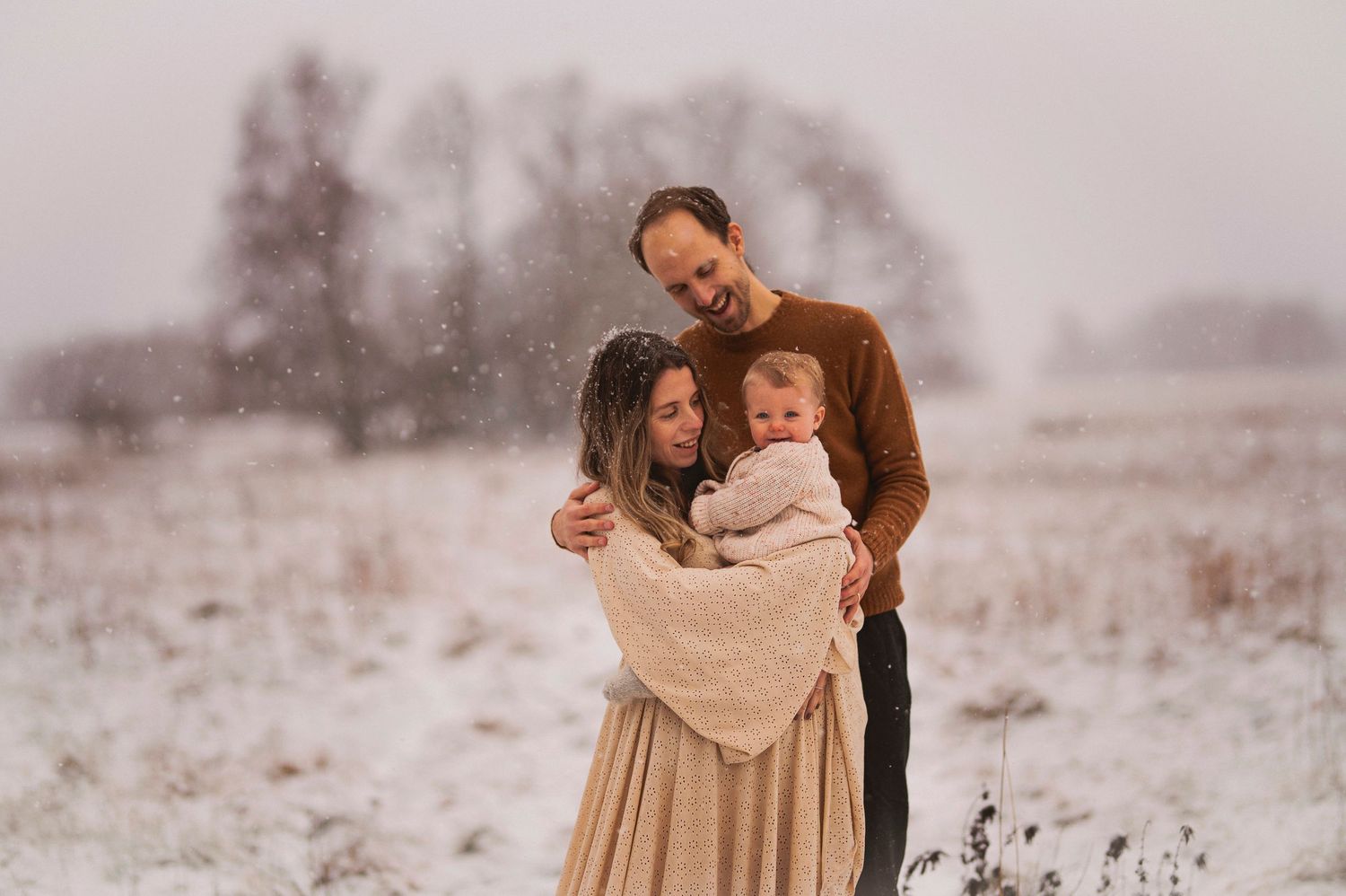 Tender family moment captured in a wintry field with falling snow.