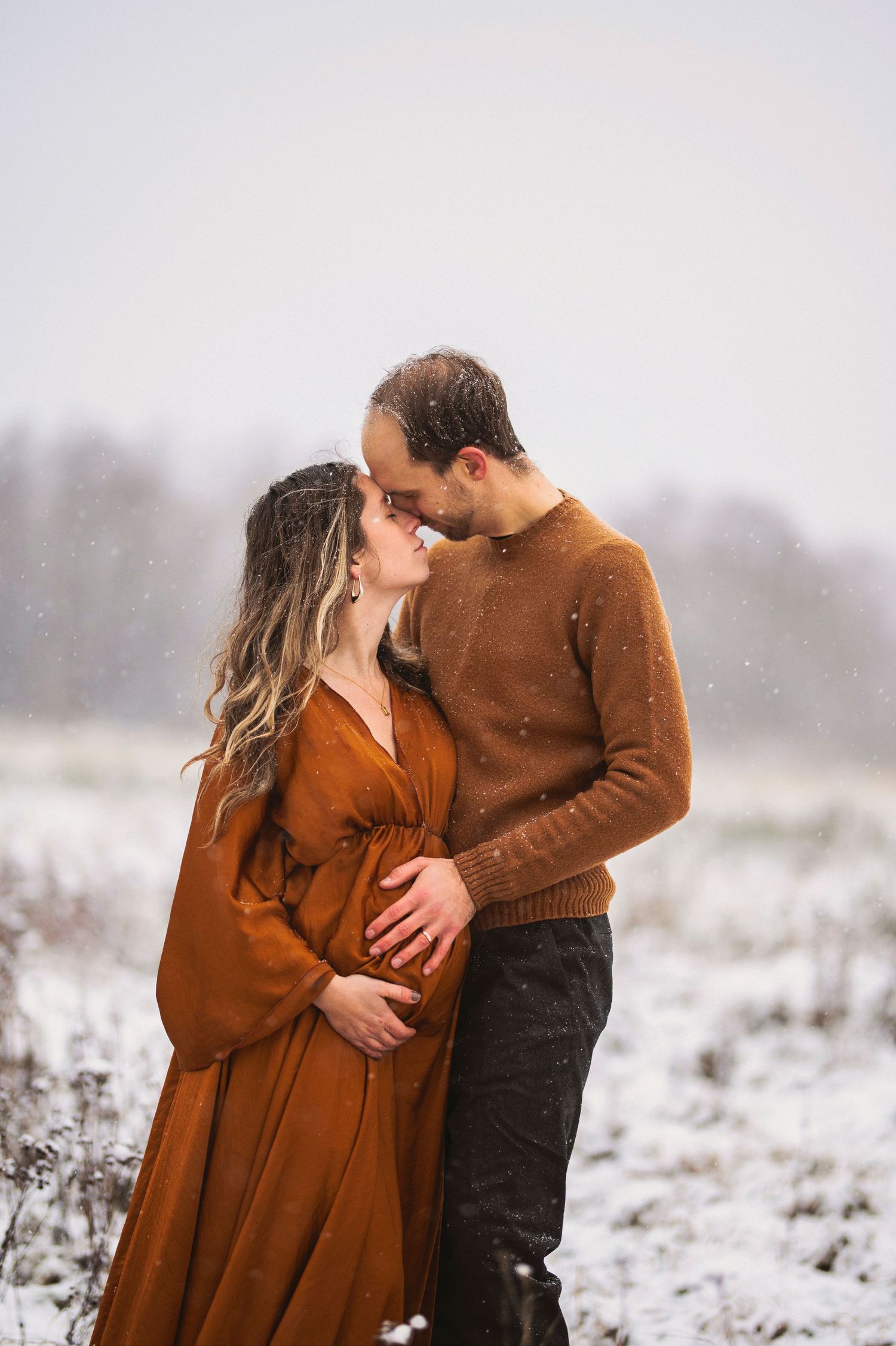 A loving winter maternity moment captured as a couple embraces in a snow-dusted field.