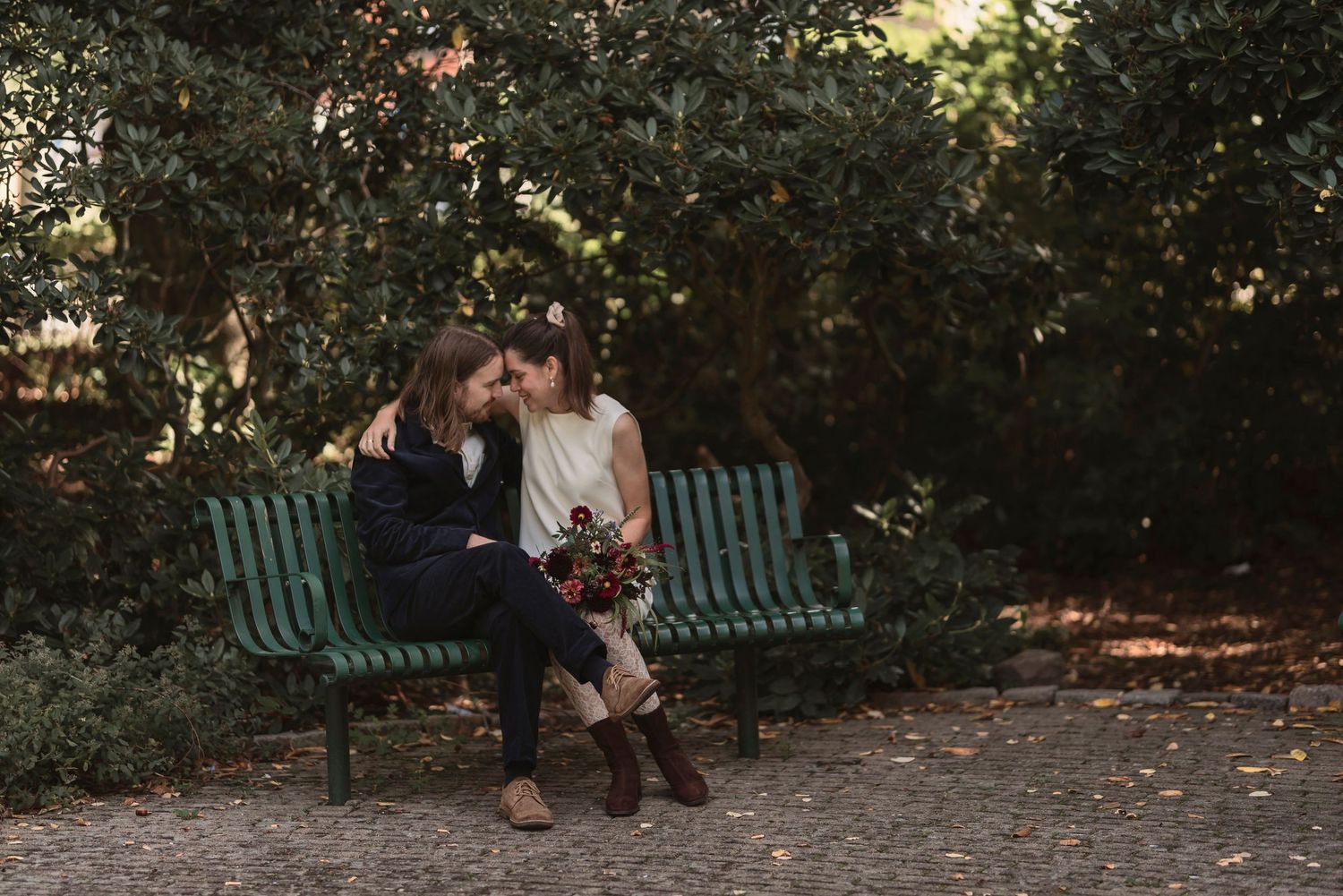 Romantic couple sitting close together on a green park bench surrounded by lush greenery.