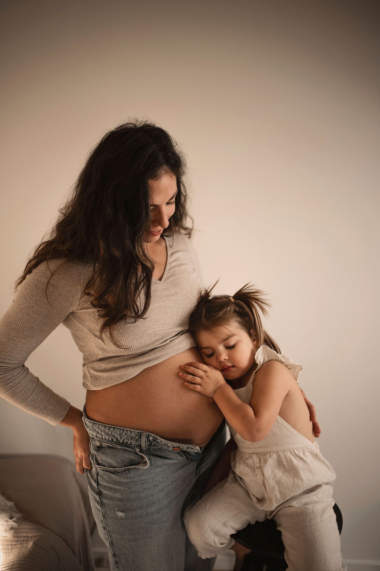 Intimate maternal moment with small child resting against pregnant belly.