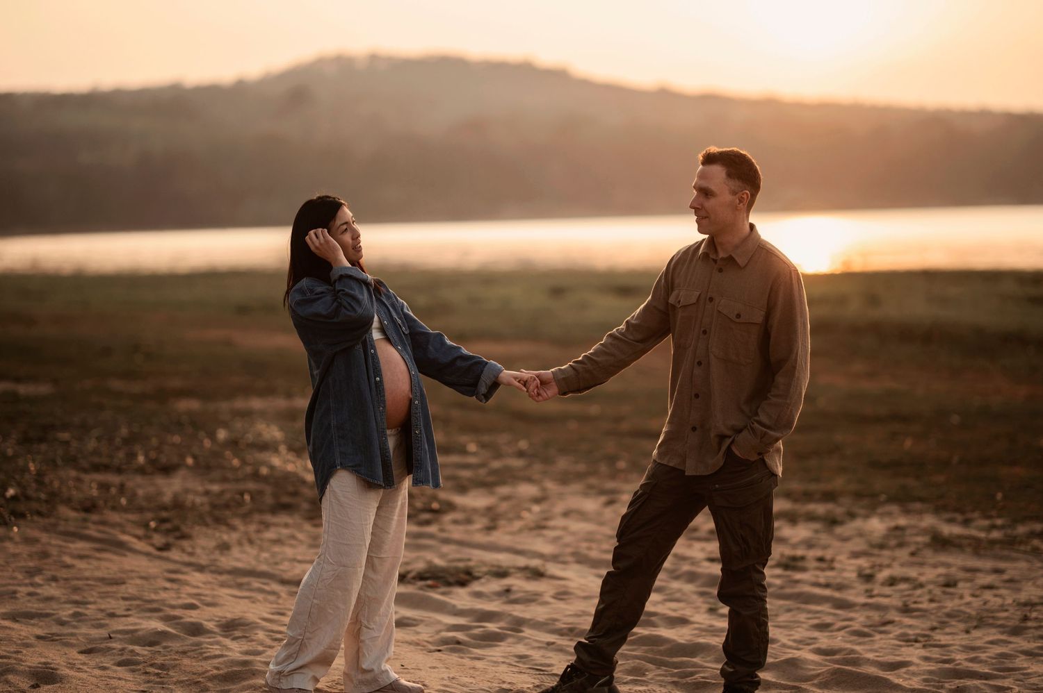 A couple shares a romantic moment on a beach at sunset while walking along the shoreline.