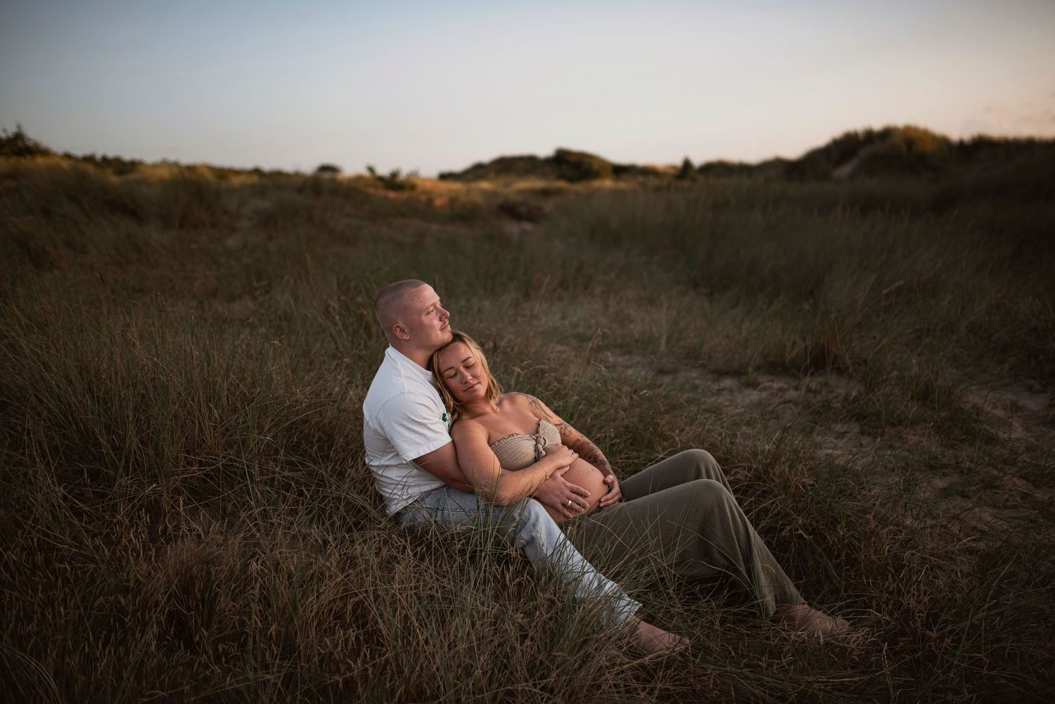 A couple embraces on a grassy hillside at sunset creating a romantic silhouette against the warm sky.