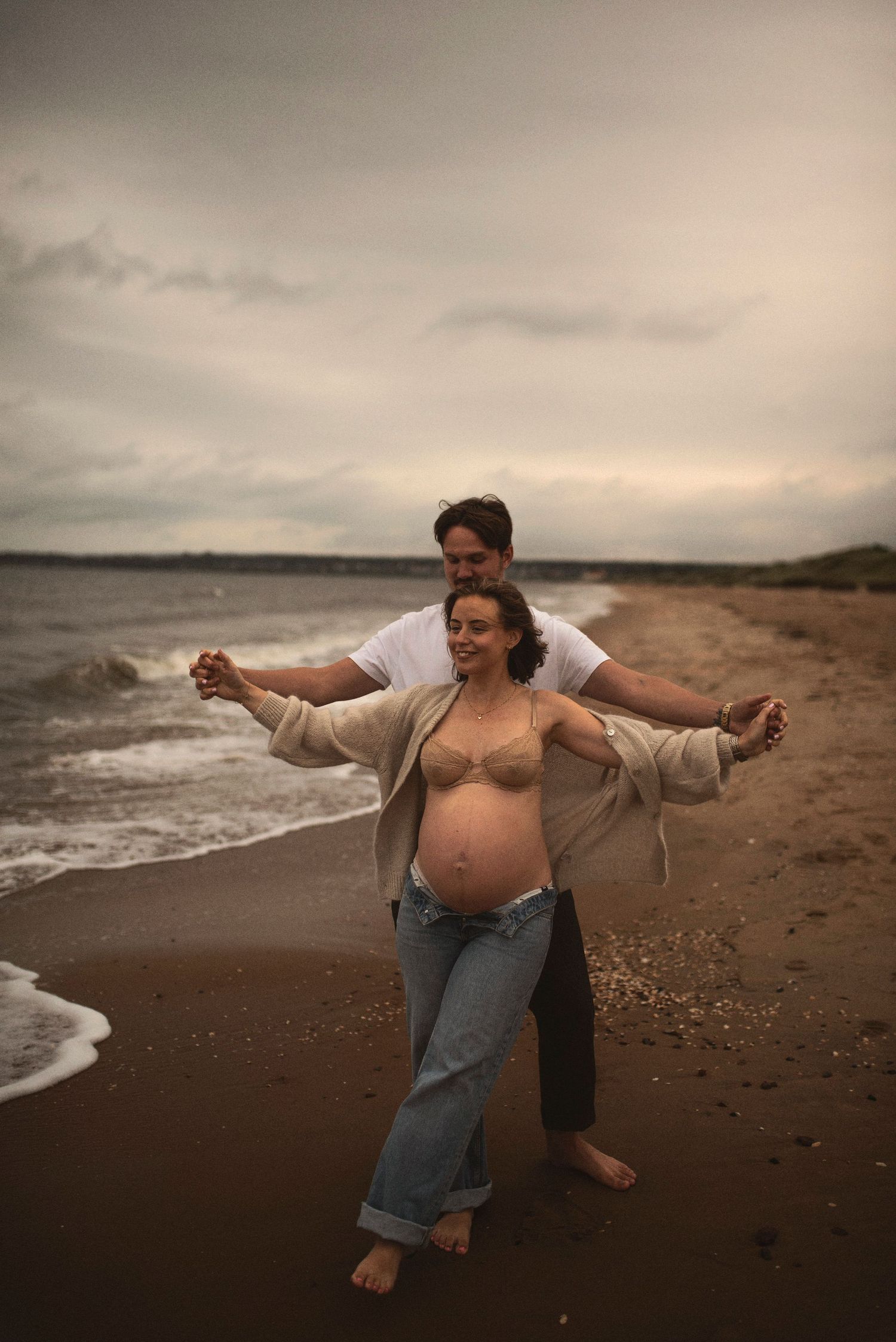 Tender moment between couple on beach as waves crash against the shore.