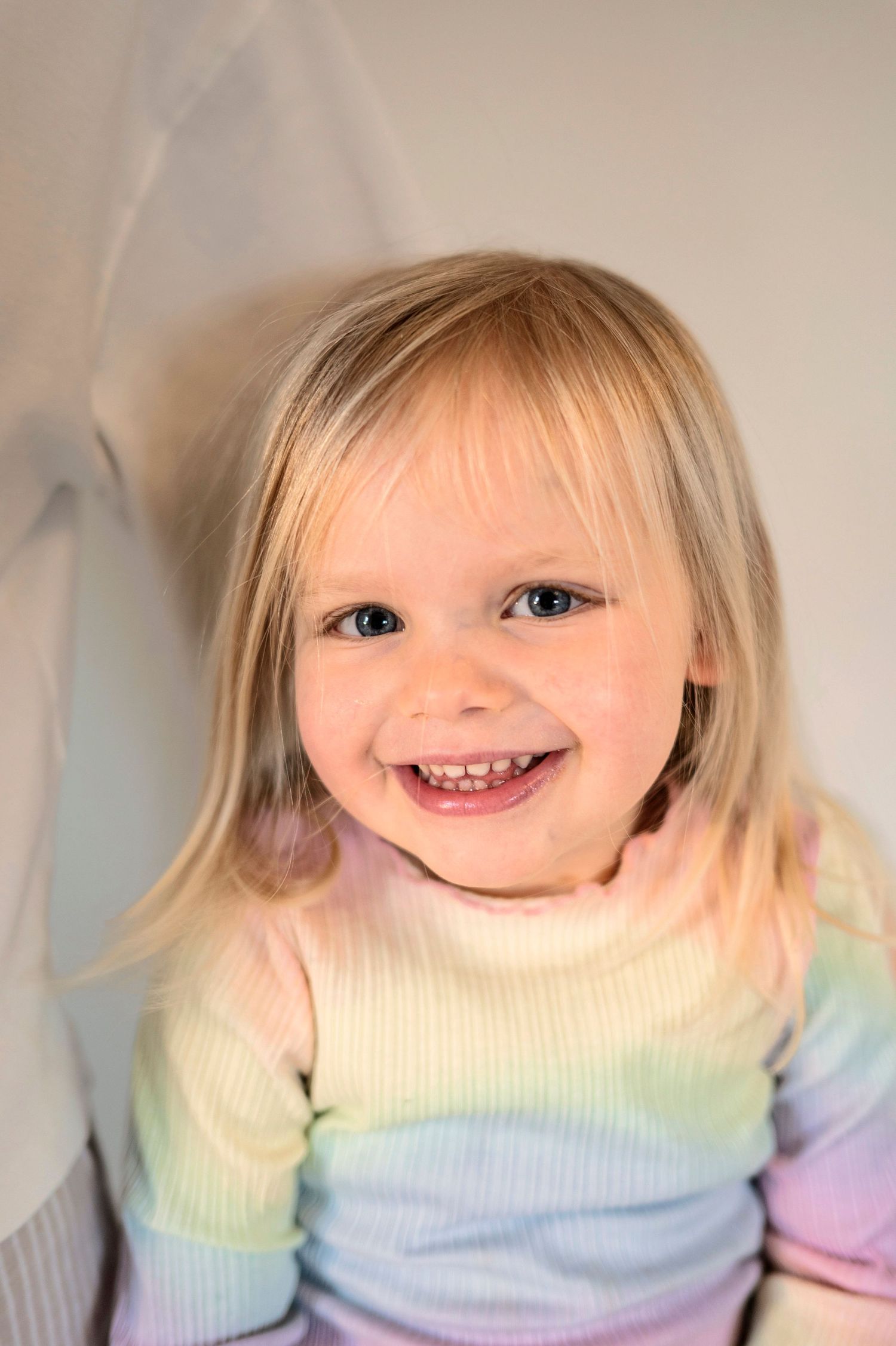 A young child wearing a pastel rainbow sweater smiles brightly at the camera.