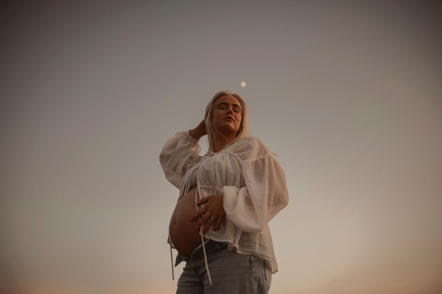 A person in a white loose blouse strikes a dramatic pose against a neutral background.