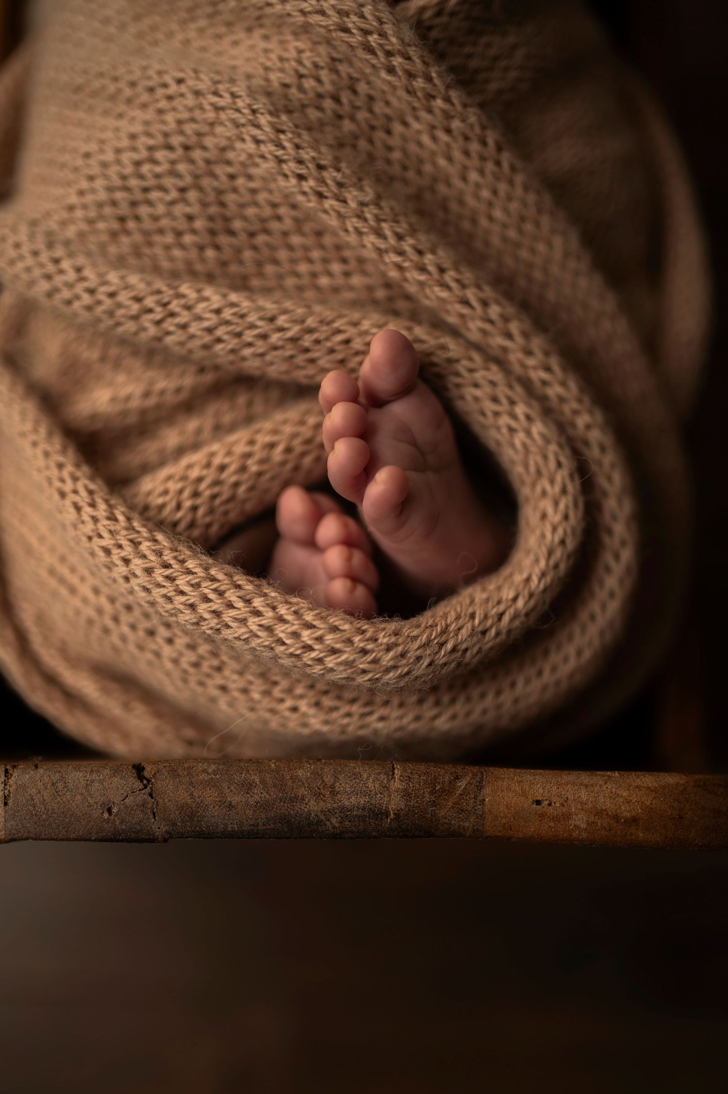 Close-up of tiny baby feet peeking out from cozy knit blanket on wooden surface.