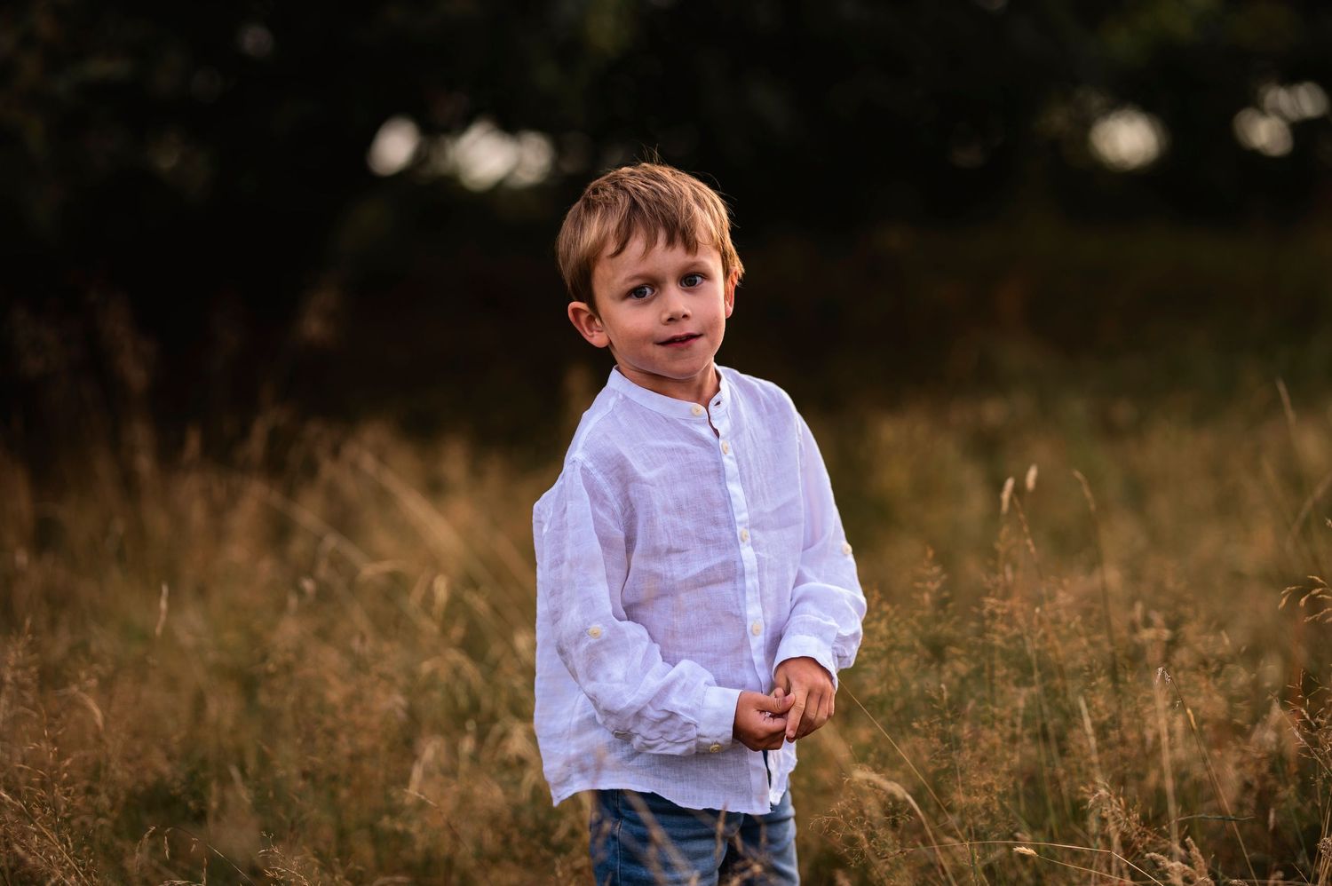 Child wearing a white shirt standing in a grassy field at dusk.