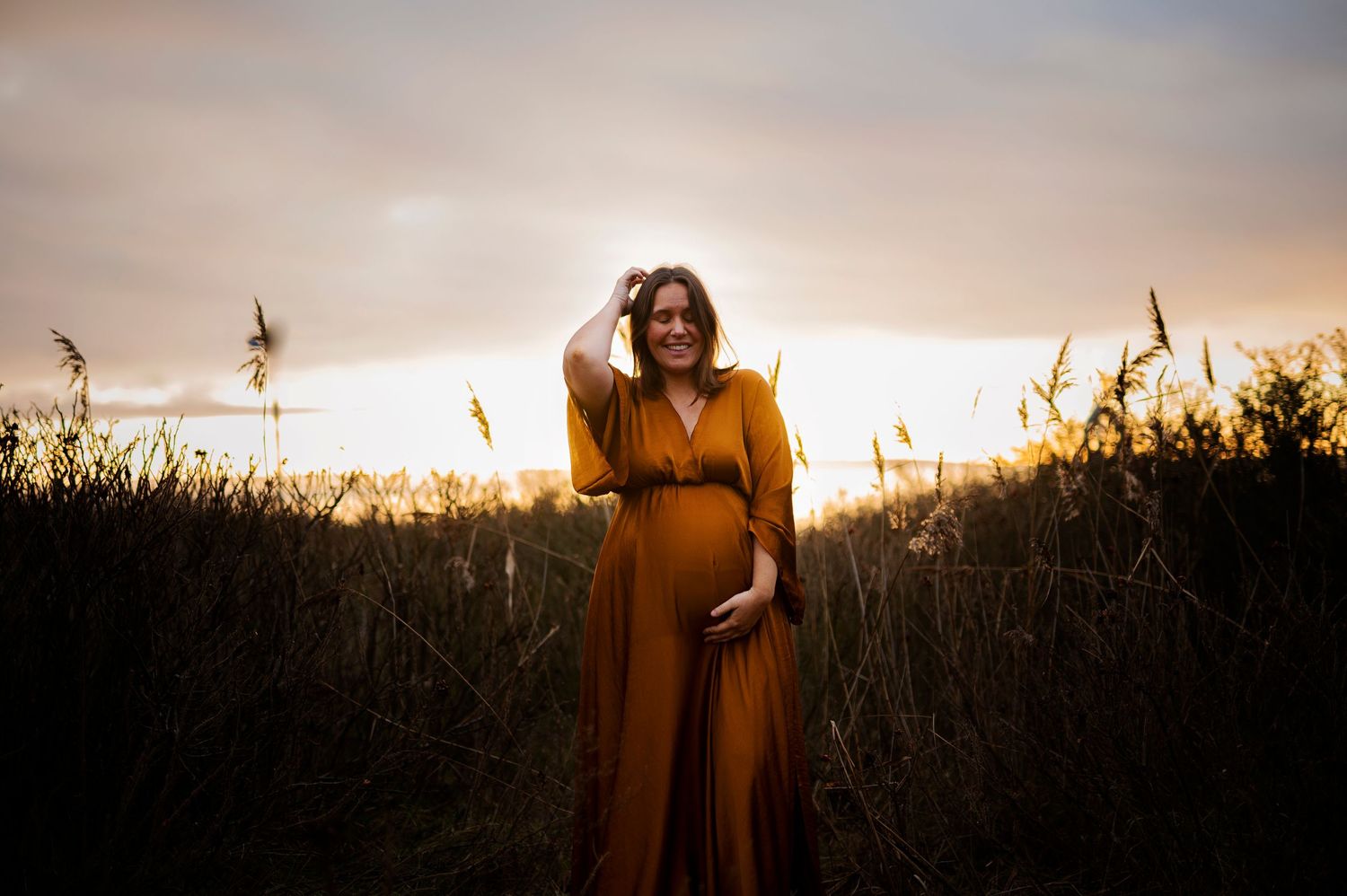 Warm sunset light illuminates figure in mustard dress among wild grasses during golden hour.