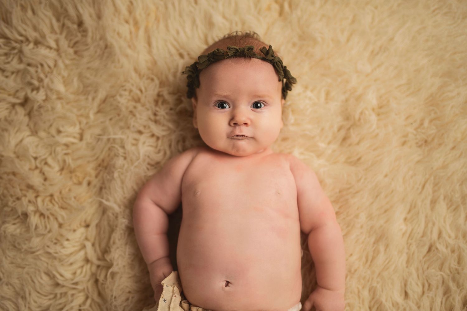 Chubby baby resting on plush beige background.