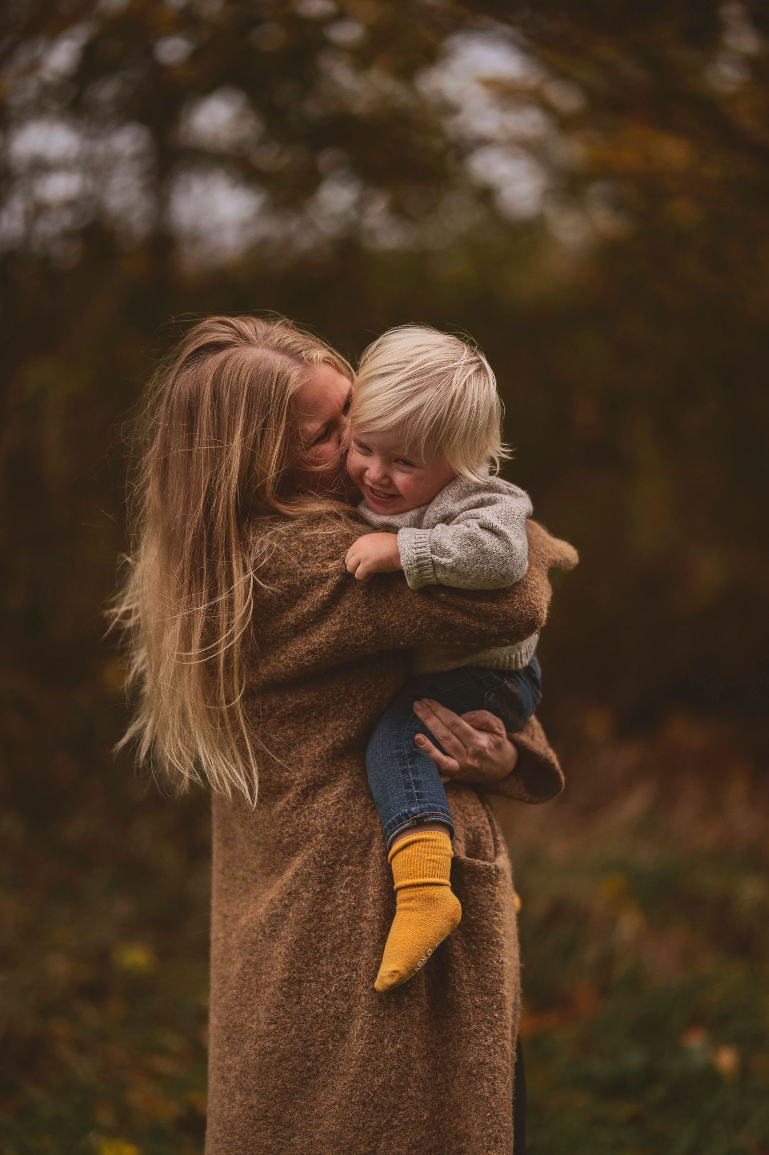 Joyful embrace between adult in brown coat and small child with yellow socks outdoors.