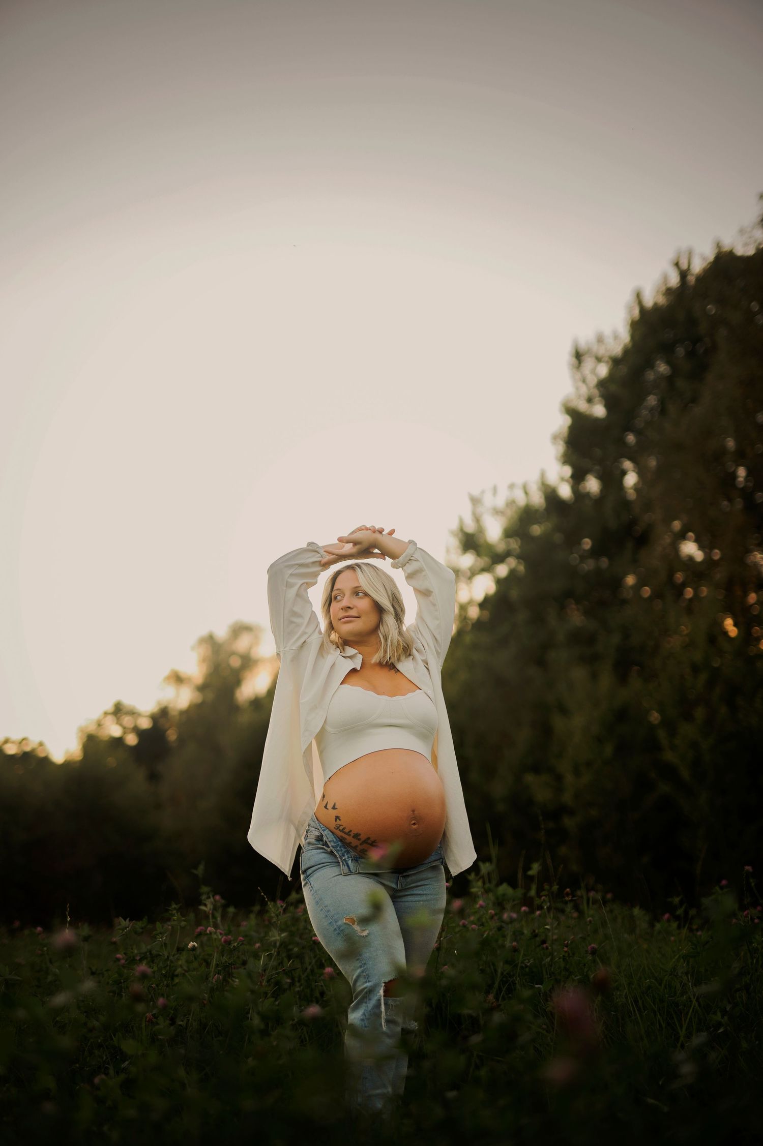 Creative pregnancy portrait with arms raised in a natural outdoor setting.