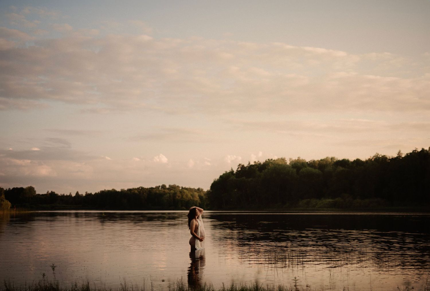 Silhouette of a person standing in a lake during sunset with trees in background.