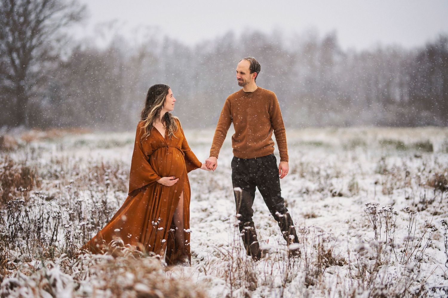 A couple shares a tender moment while standing in a snow-covered field during a maternity photoshoot.