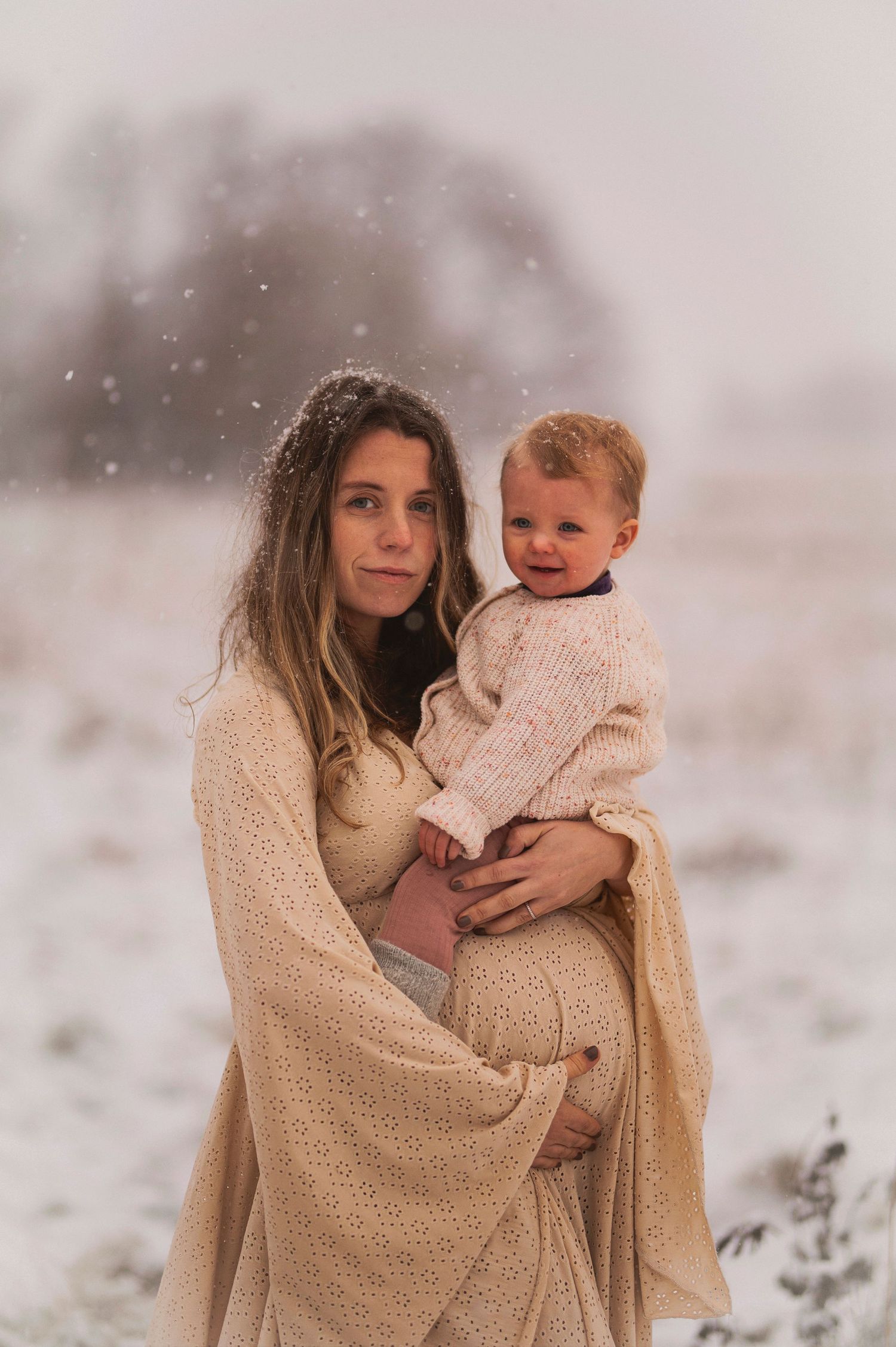 Mother and child portrait in a snowy setting wearing cream-colored clothing.