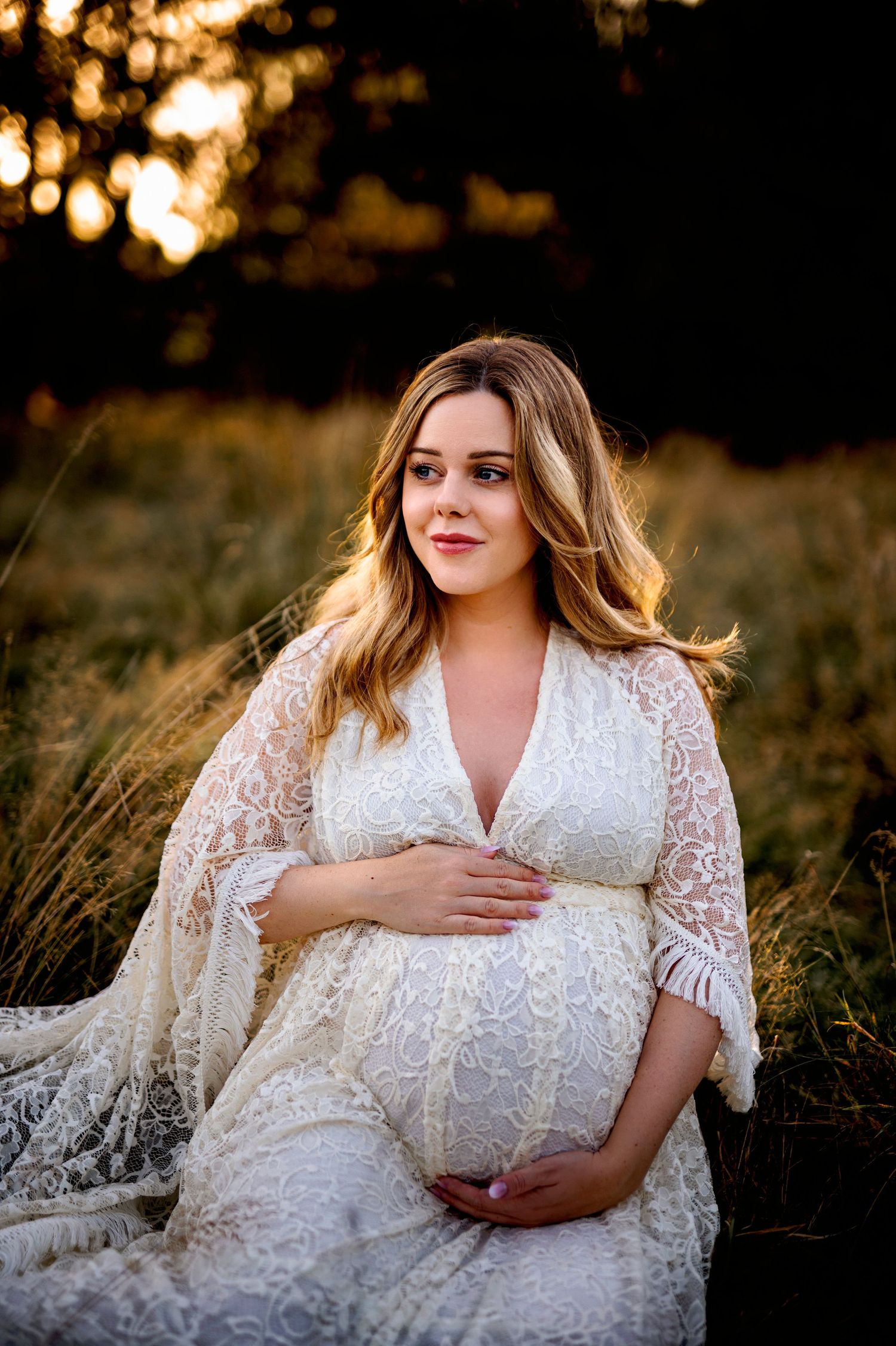 Serene maternity portrait in delicate white lace dress during golden sunset.