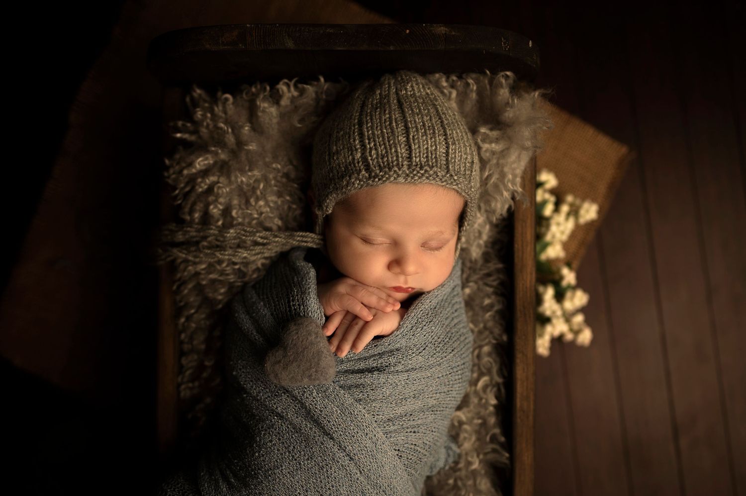 Peaceful newborn sleeping in gray wrap and knit hat with decorative snowflakes.