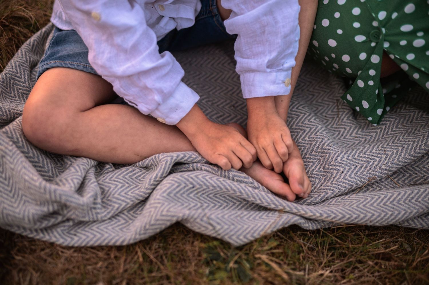 Bare feet resting on a gray blanket in the grass during golden hour.
