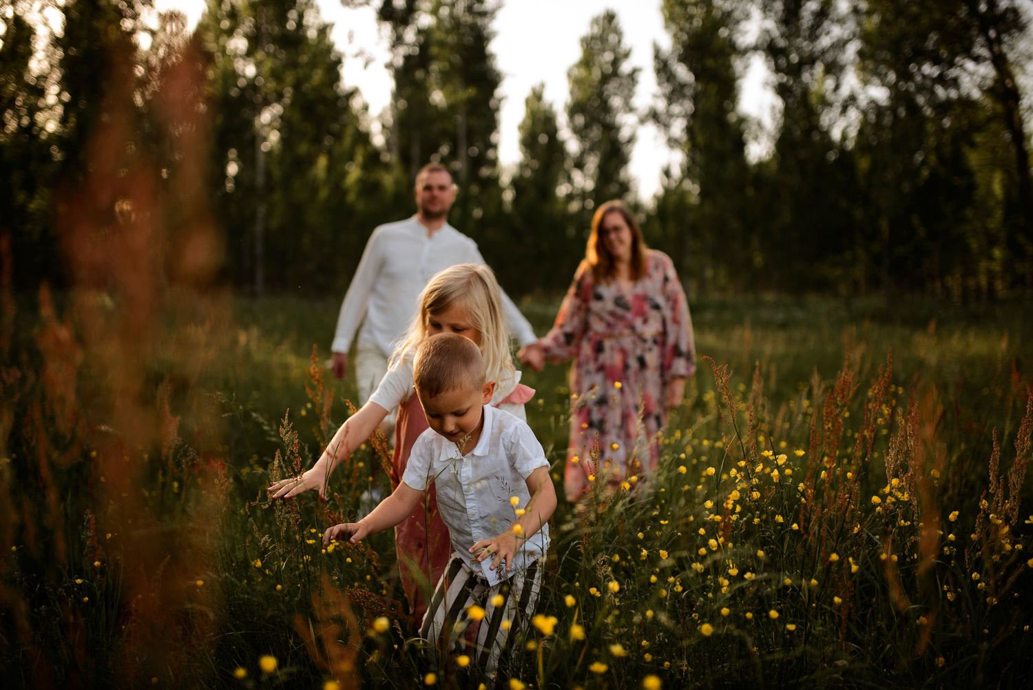 Children run through wildflowers while parents follow behind in golden field.