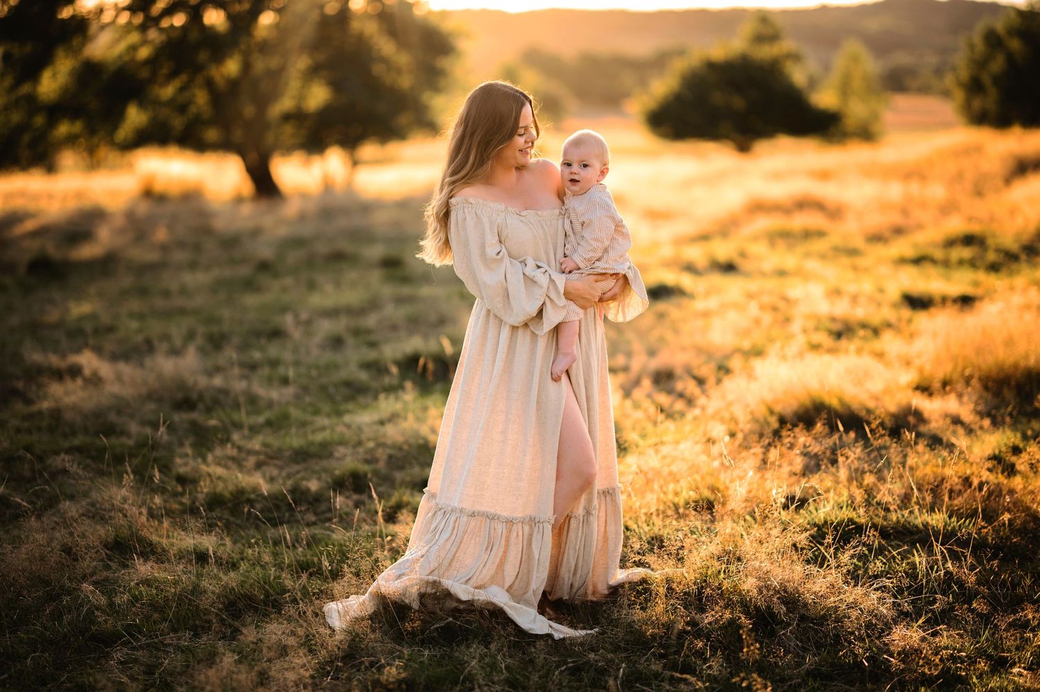 Ethereal portrait in flowing cream dress against golden sunset landscape.