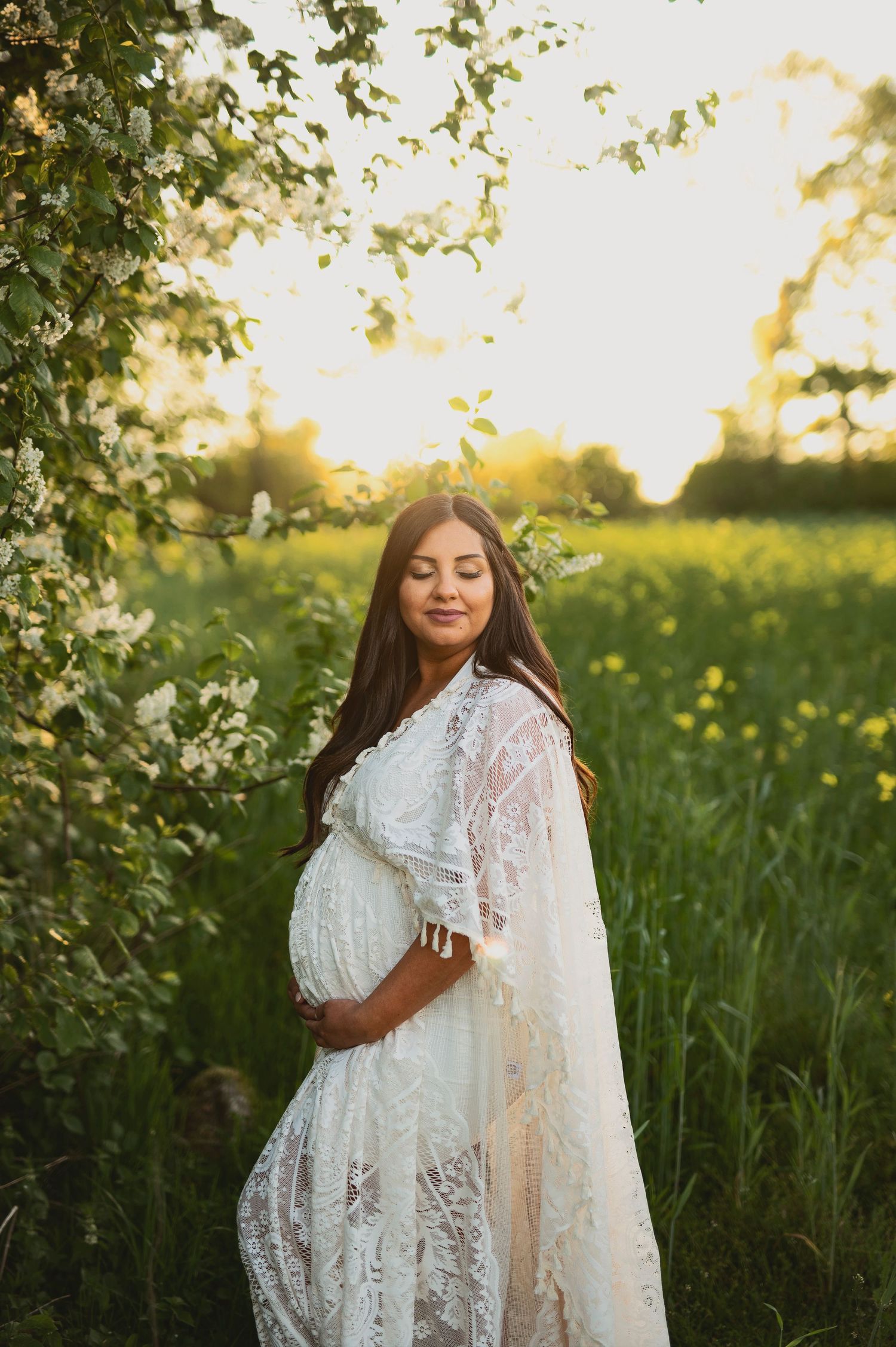 Serene maternity photo featuring woman in white lace gown surrounded by spring blooms.