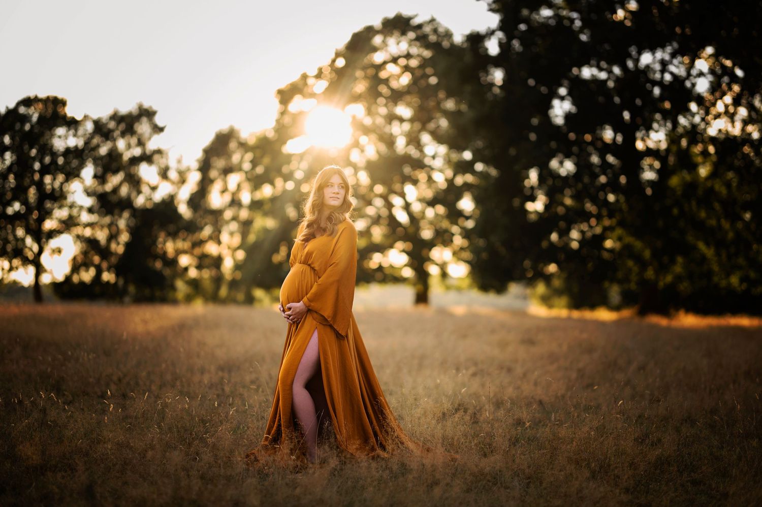 Silhouetted figure in mustard dress twirls in sunlit meadow during golden hour.