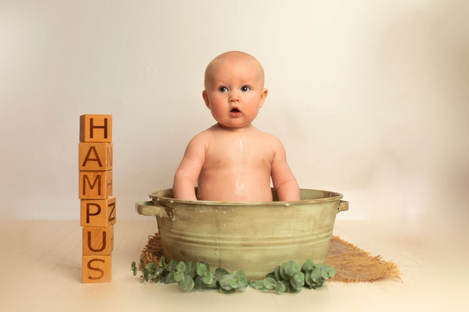 Baby in vintage basin with wooden alphabet blocks spelling HAMPUS.