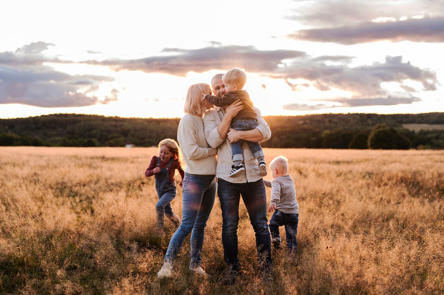 Family embracing in tall grass field during dramatic sunset.