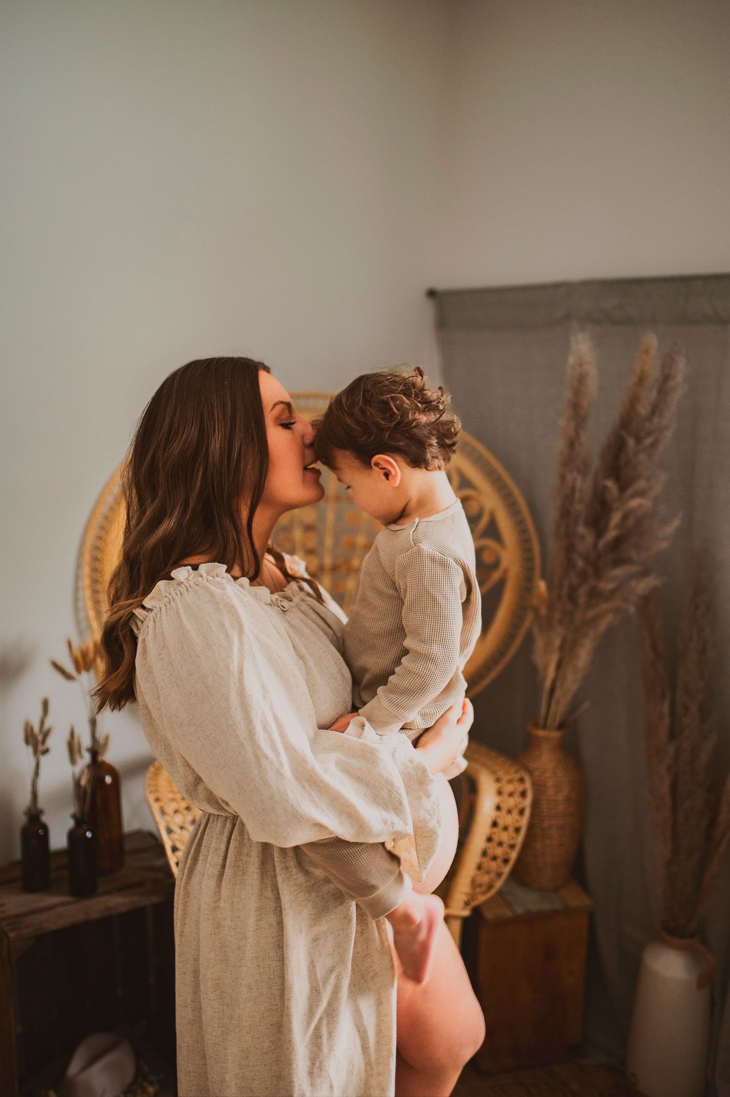 Tender maternity moment captured in front of woven peacock chair with dried pampas grass decor.