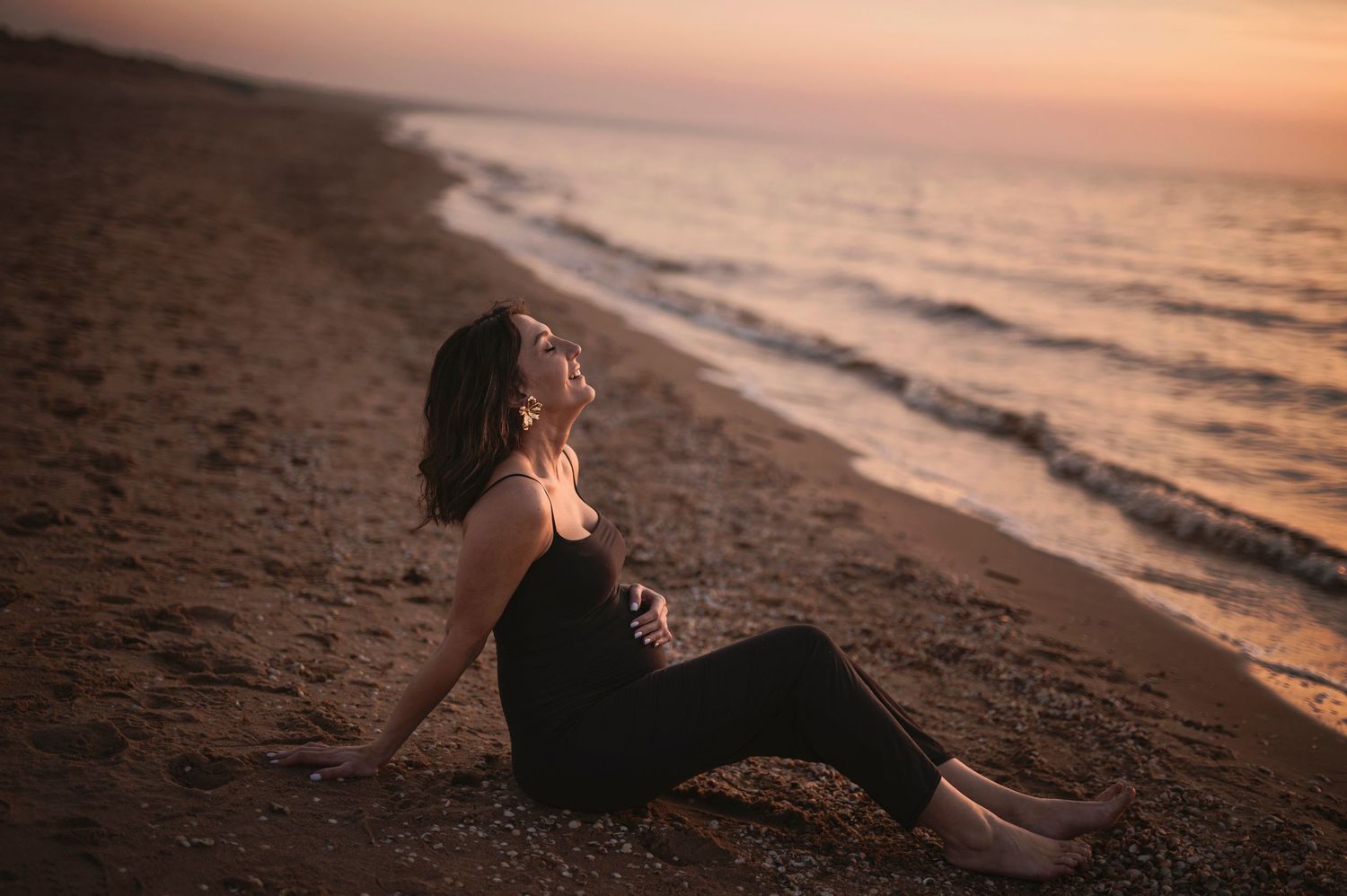 Silhouette figure relaxes on sandy beach during golden sunset as waves roll onto shore.