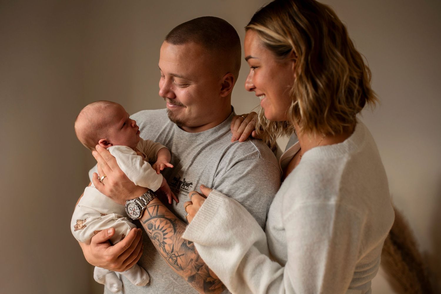A series of candid family photos showing tender moments between parents and their newborn baby in warm lighting.