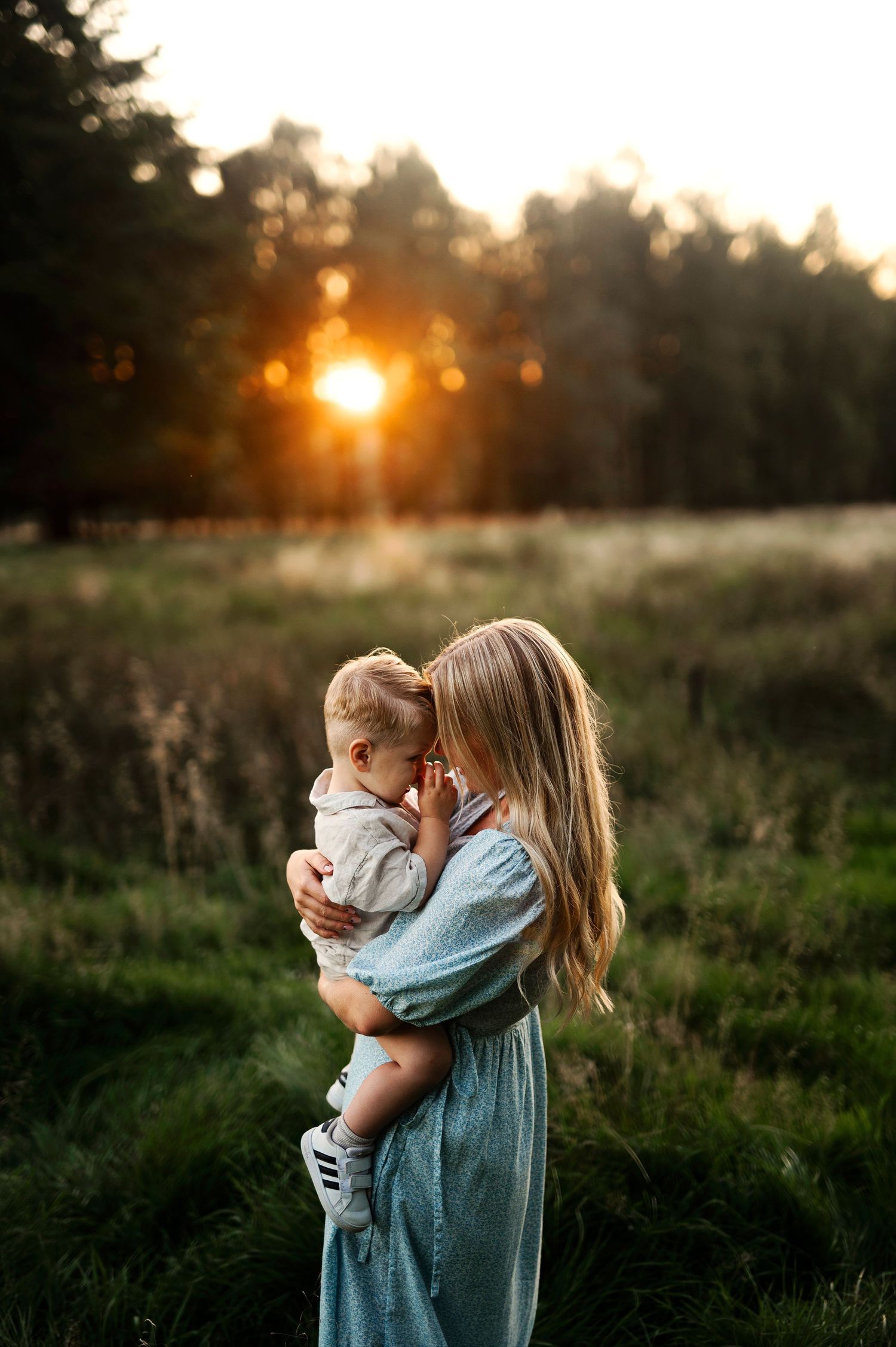 A loving embrace is captured in a meadow during golden hour with trees in the background.