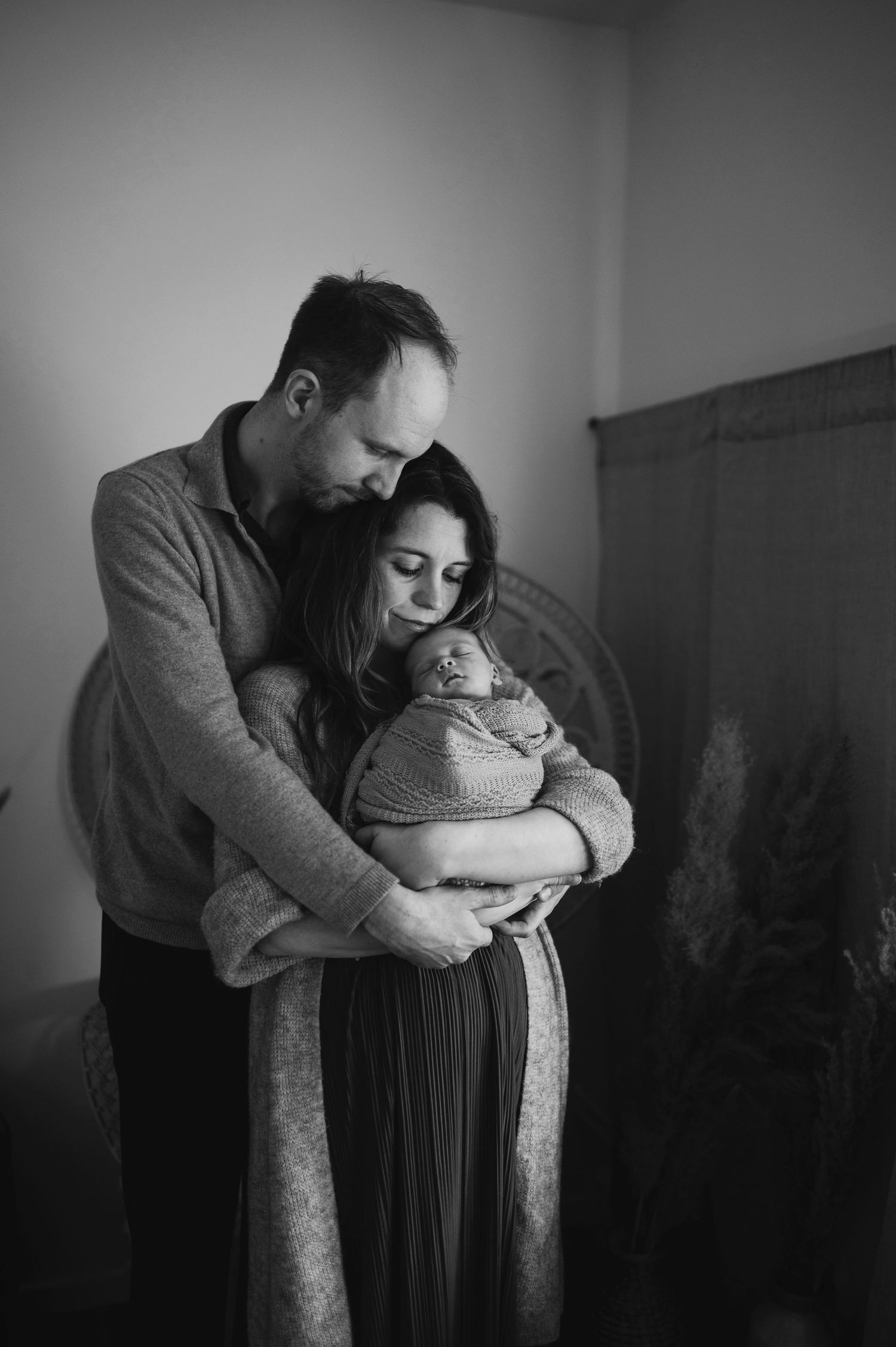 Tender black and white portrait of new parents embracing while holding their newborn.