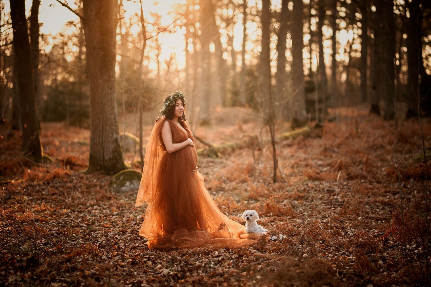 A flowing orange dress catches golden sunlight in an autumn forest during sunset.