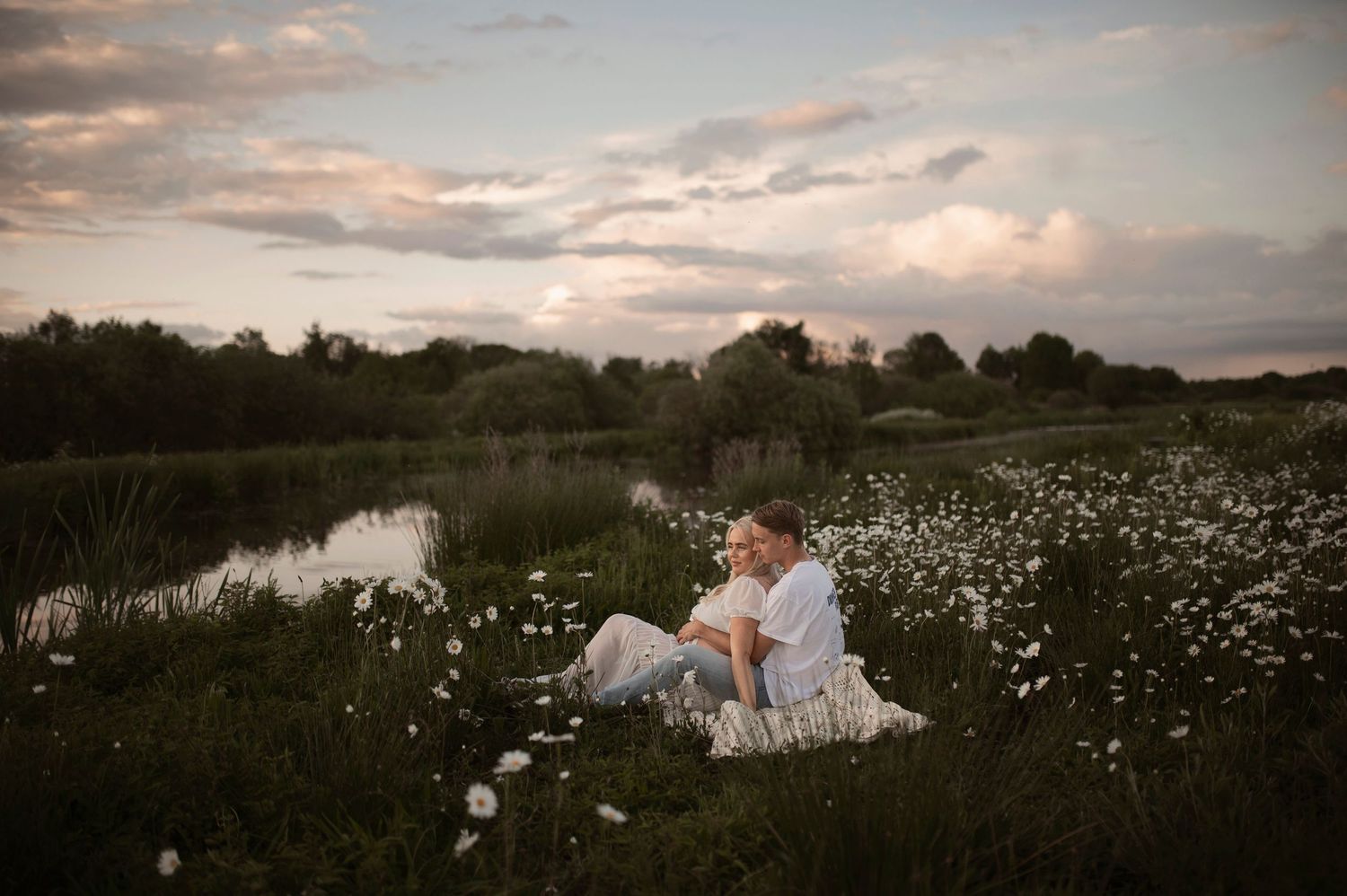 Serene sunset maternity photoshoot in rustic field filled with blooming white wildflowers.