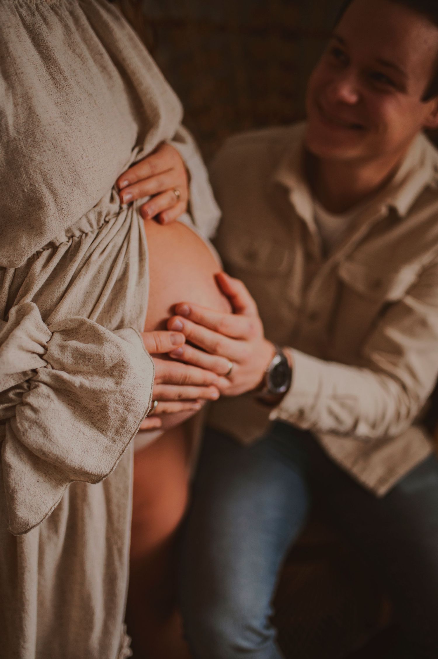 Warm-toned maternity photo showing gentle hands cradling pregnant belly in natural light.