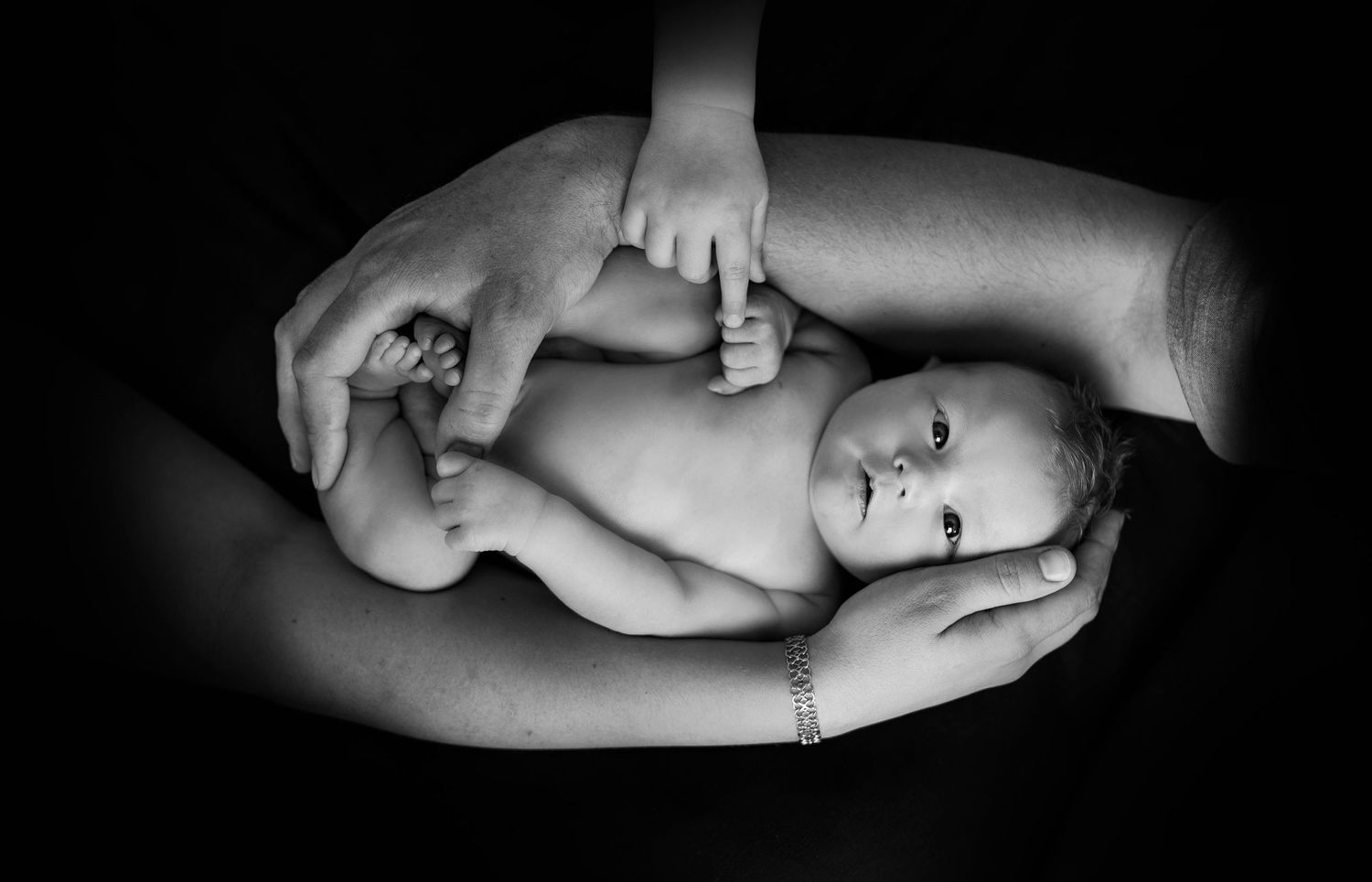 Black and white artistic portrait of infant cradled in gentle hands.