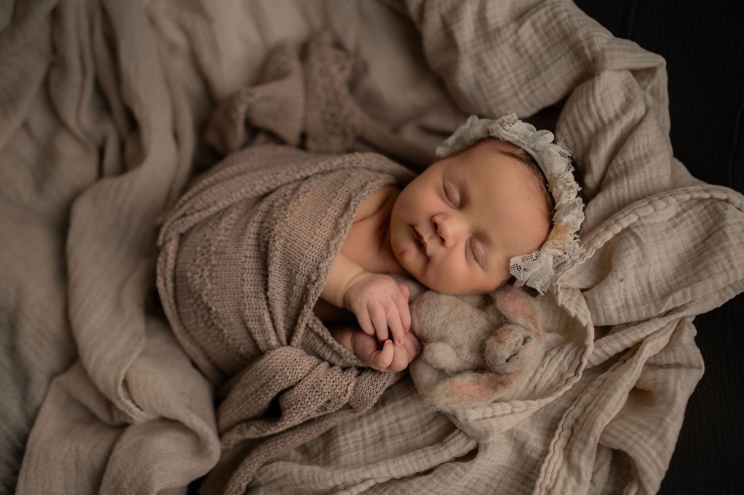 Peaceful newborn sleeping on soft beige blankets while wearing a knit wrap and matching headband.