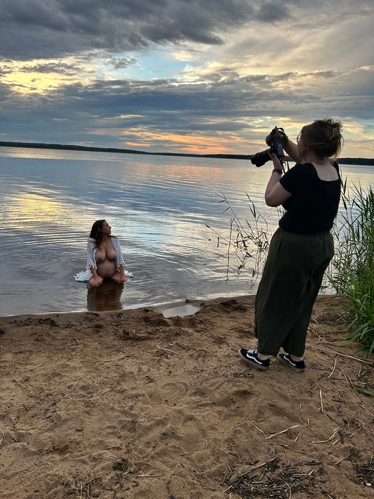 Photographer capturing a woman wading in a lake at sunset on a sandy shoreline.