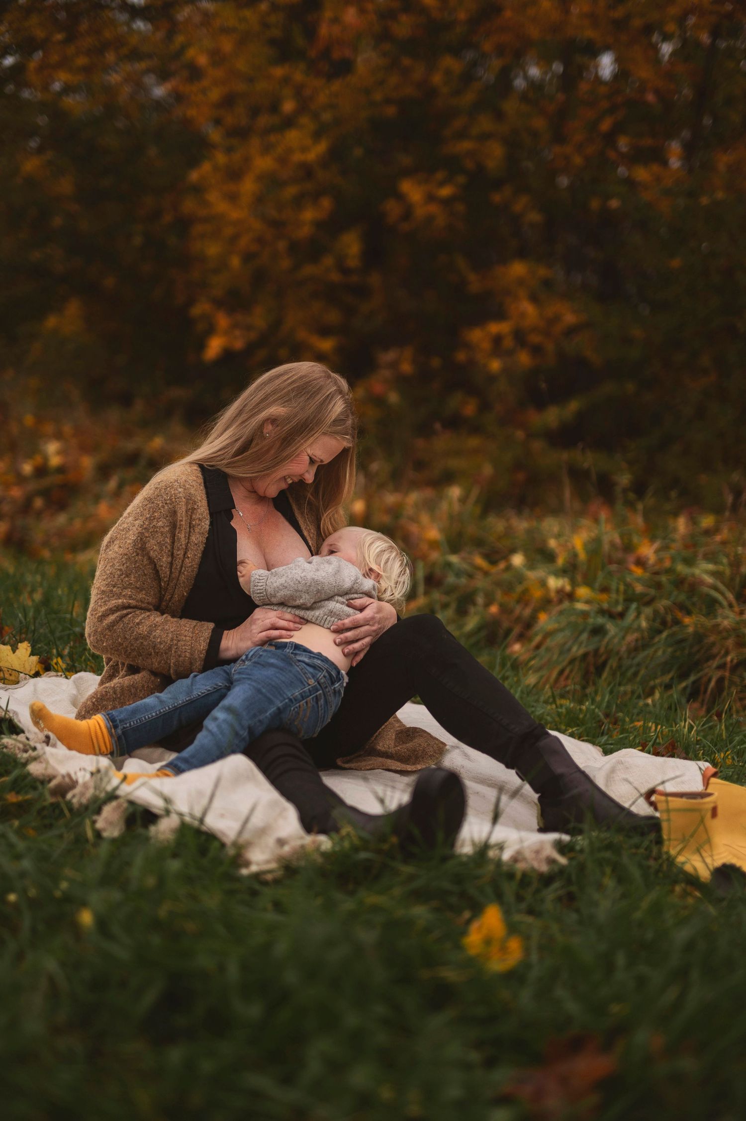 Peaceful outdoor nursing session on a white blanket surrounded by fall colors and yellow flowers.