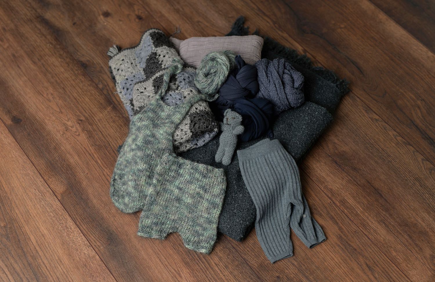 Collection of gray and blue baby clothing items displayed on hardwood floor.