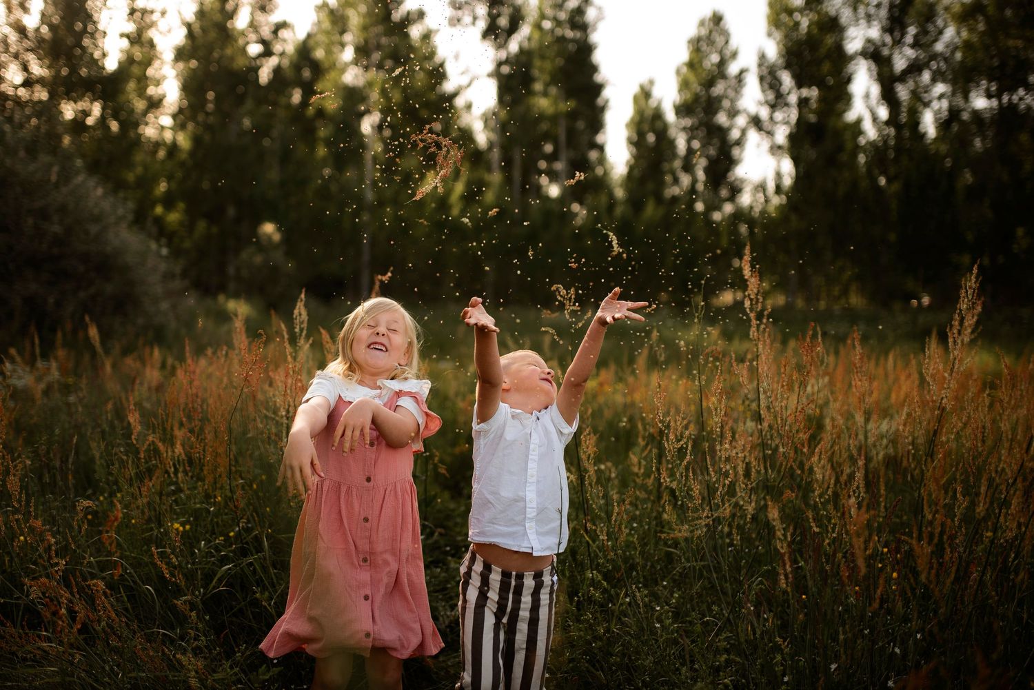 Two children playing joyfully in tall grass during sunset.