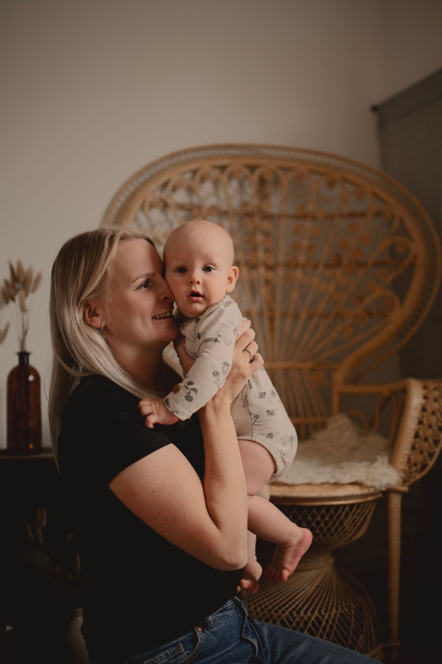 Sweet interaction between parent and infant beside a vintage peacock chair in warm lighting.