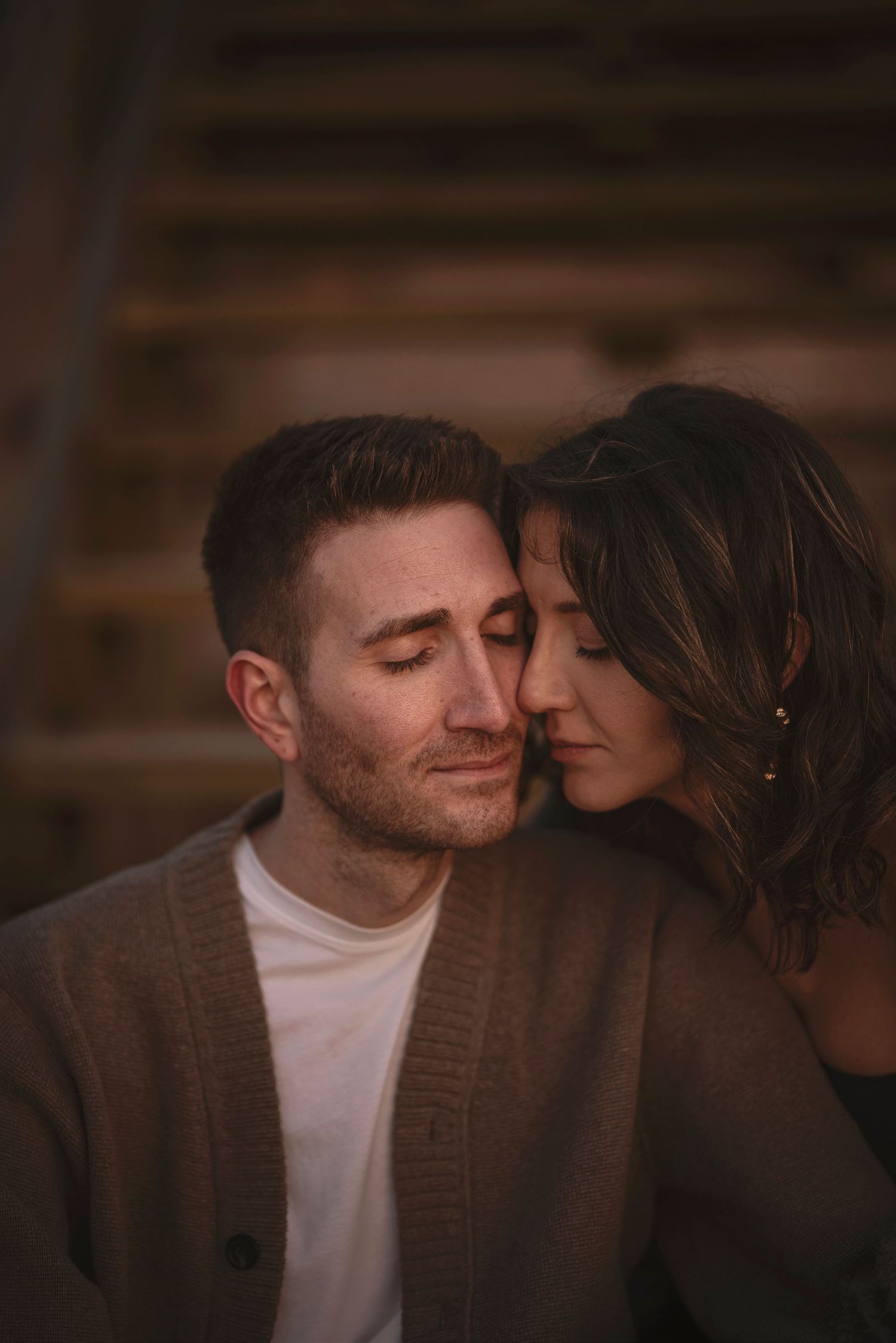 Intimate couple sharing tender moment together in warm lighting against wooden backdrop.