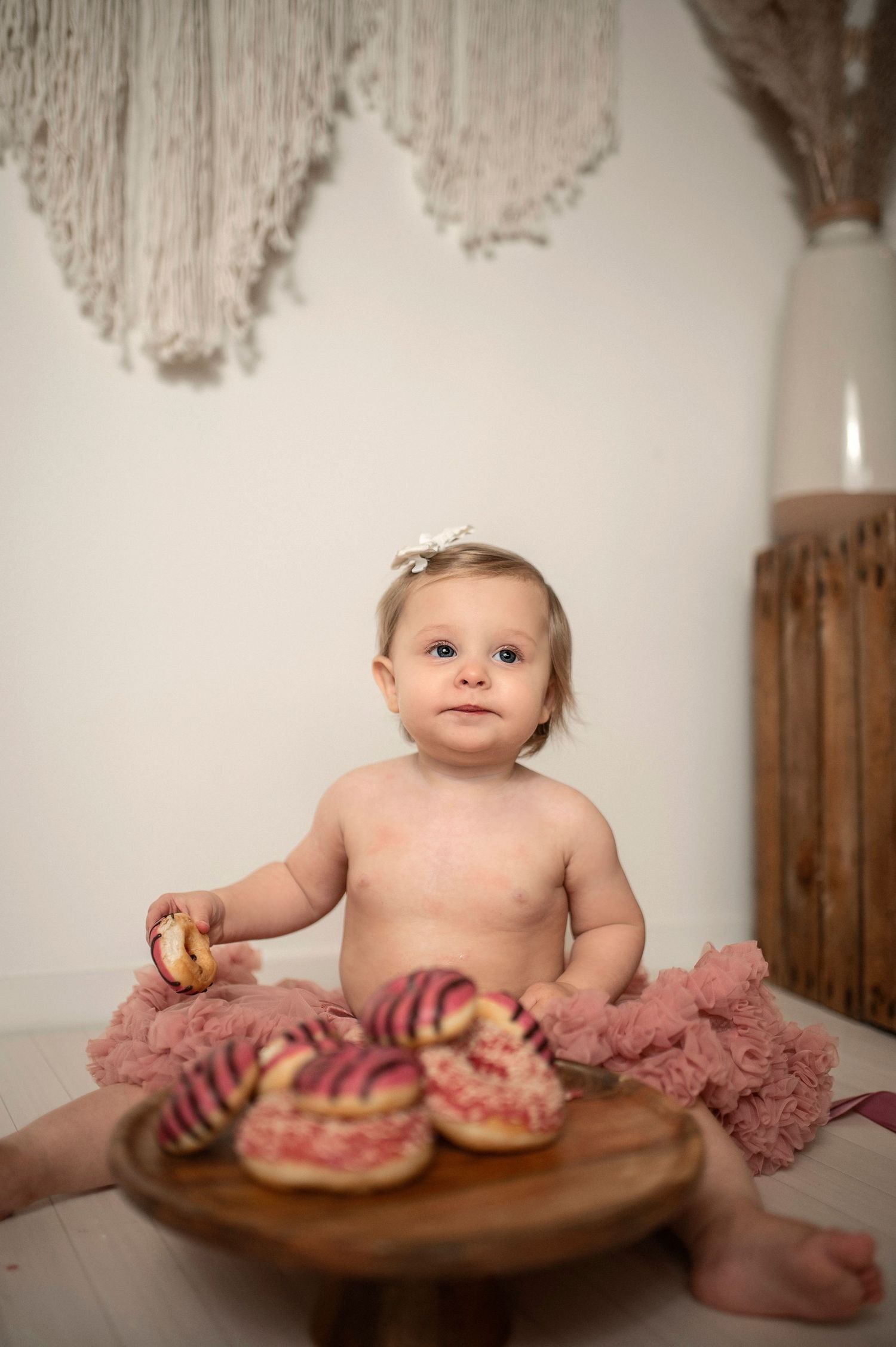 A sweet milestone photo series showing a baby with donuts on a wooden surface against a white backdrop.