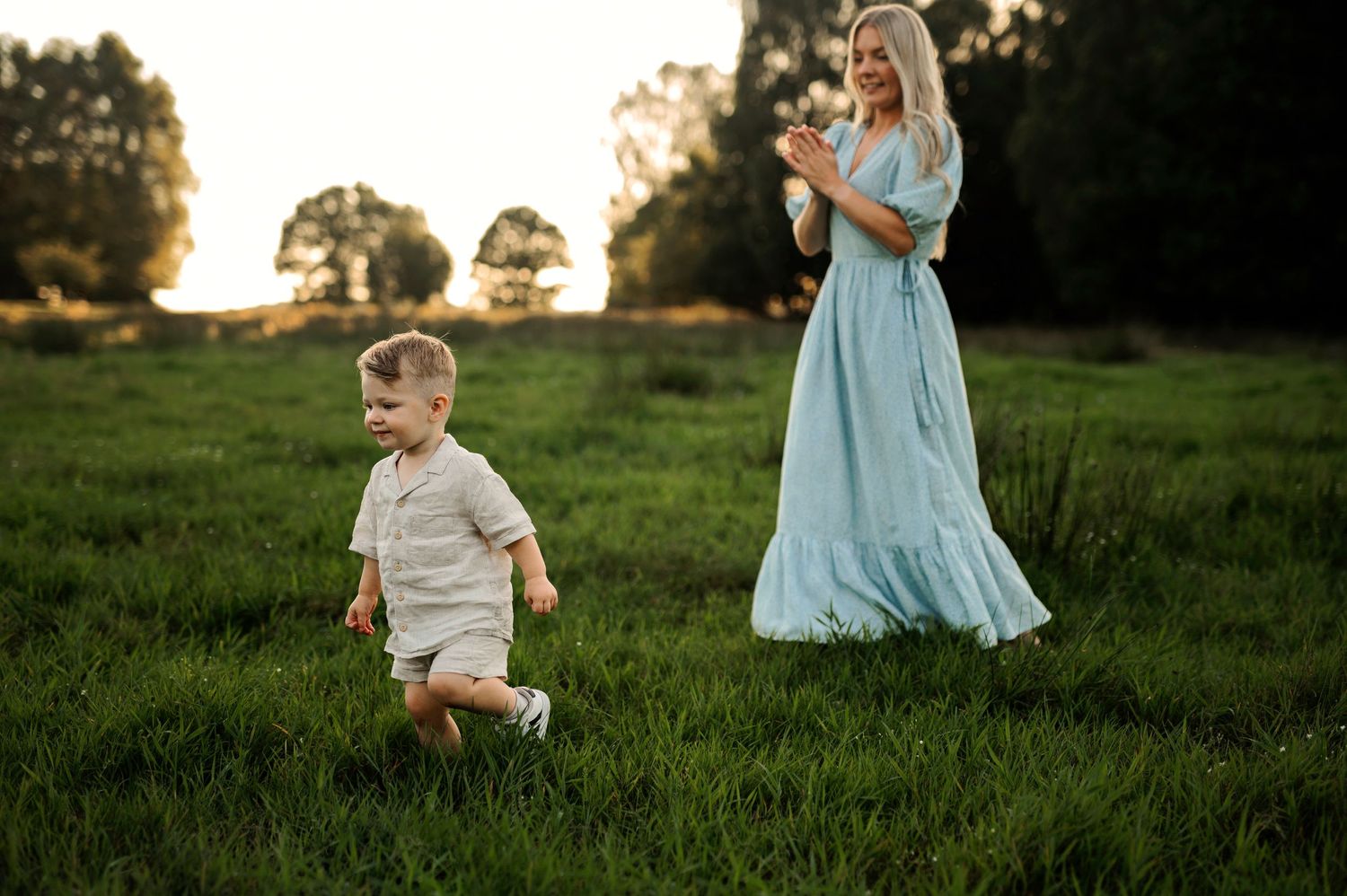 A playful scene in a grassy field with a running child and someone in a light blue dress.